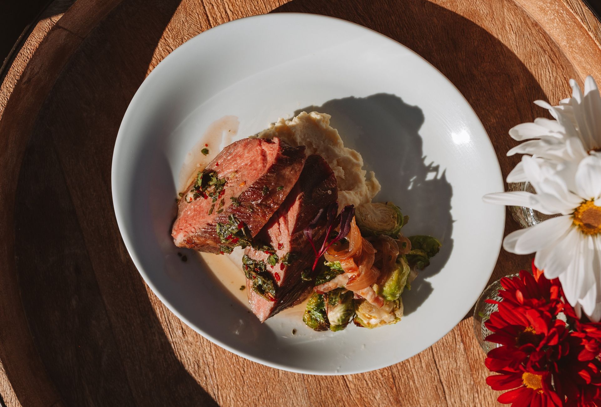 Sliced steak with mashed potatoes and Brussels sprouts on a white plate, garnished with herbs.