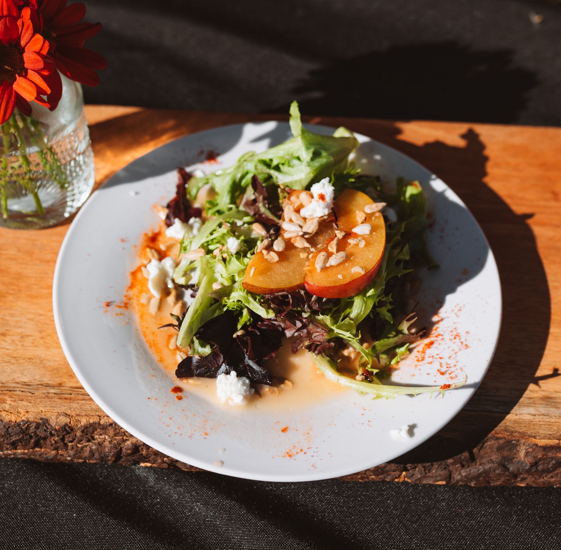 Salad with peach slices, greens, and nuts on a white plate on a wooden table.