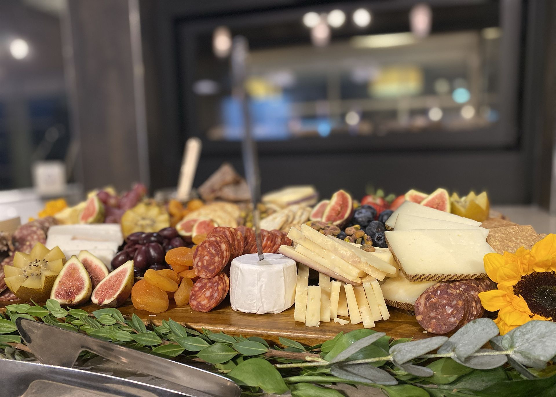 Charcuterie board: cheeses, meats, fruits, nuts, and crackers on a wooden platter, with greenery.