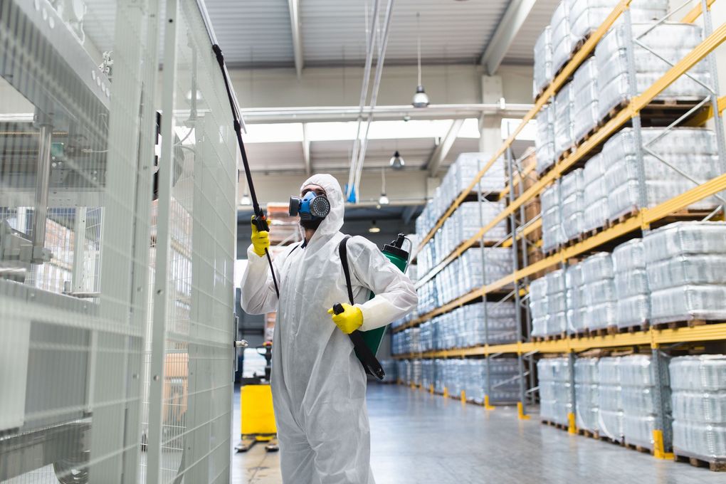 A man in a protective suit is spraying a warehouse with a sprayer.