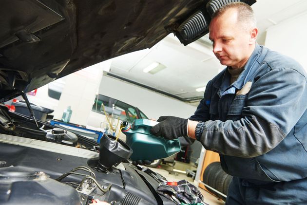 Mechanic working under a car hood in a garage, wearing gloves and inspecting engine parts.