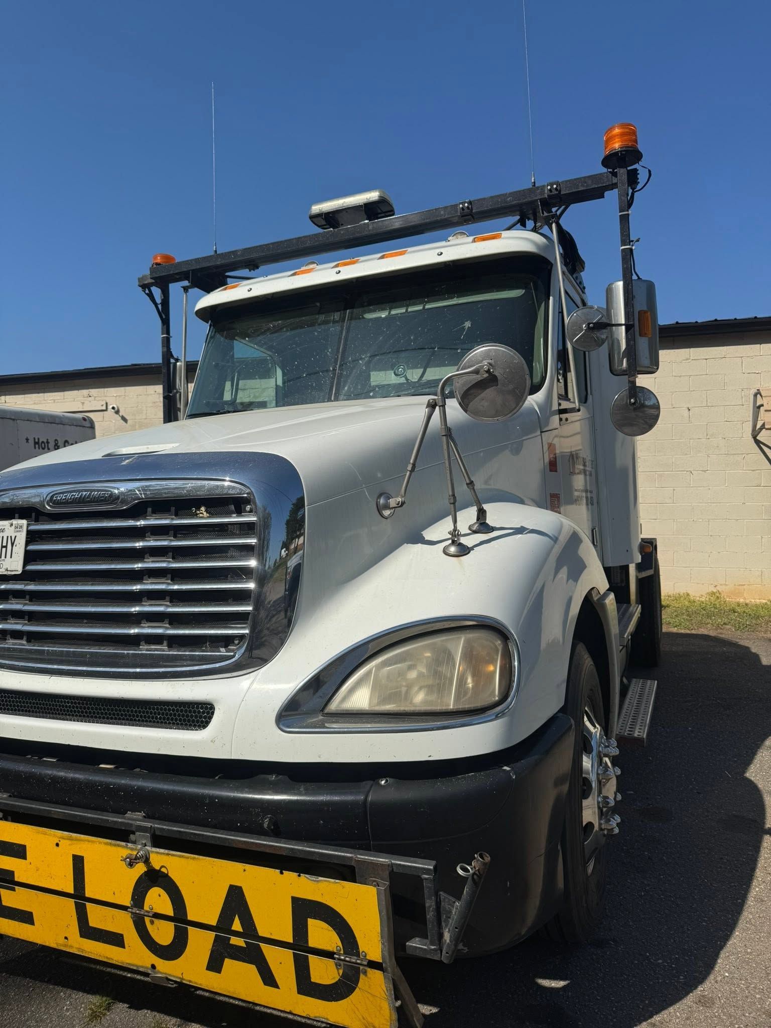 White tow truck with yellow “LOAD” sign parked outdoors under a clear blue sky