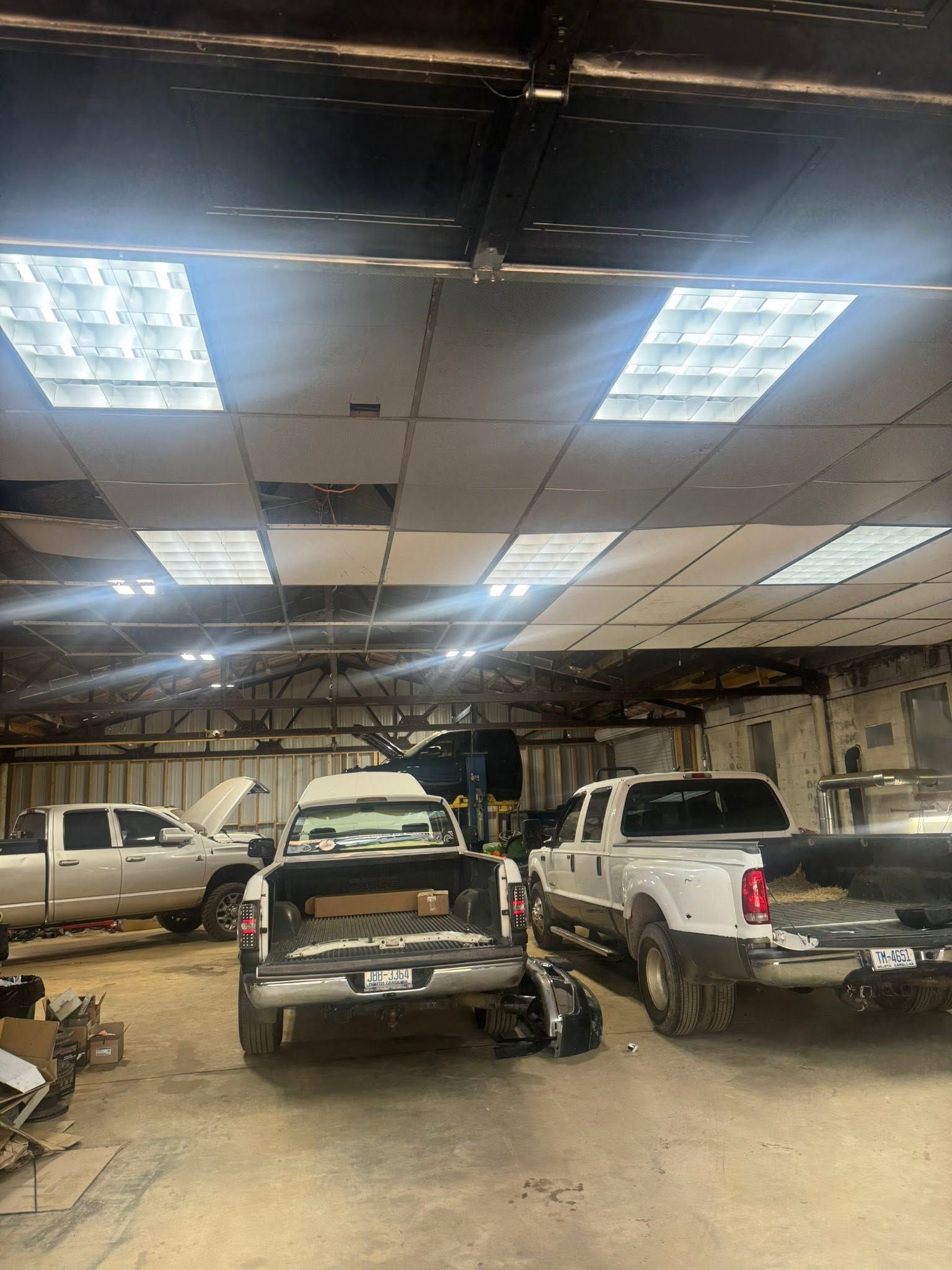 Indoor garage with several pickup trucks parked under bright ceiling lights and a trailer in the center.