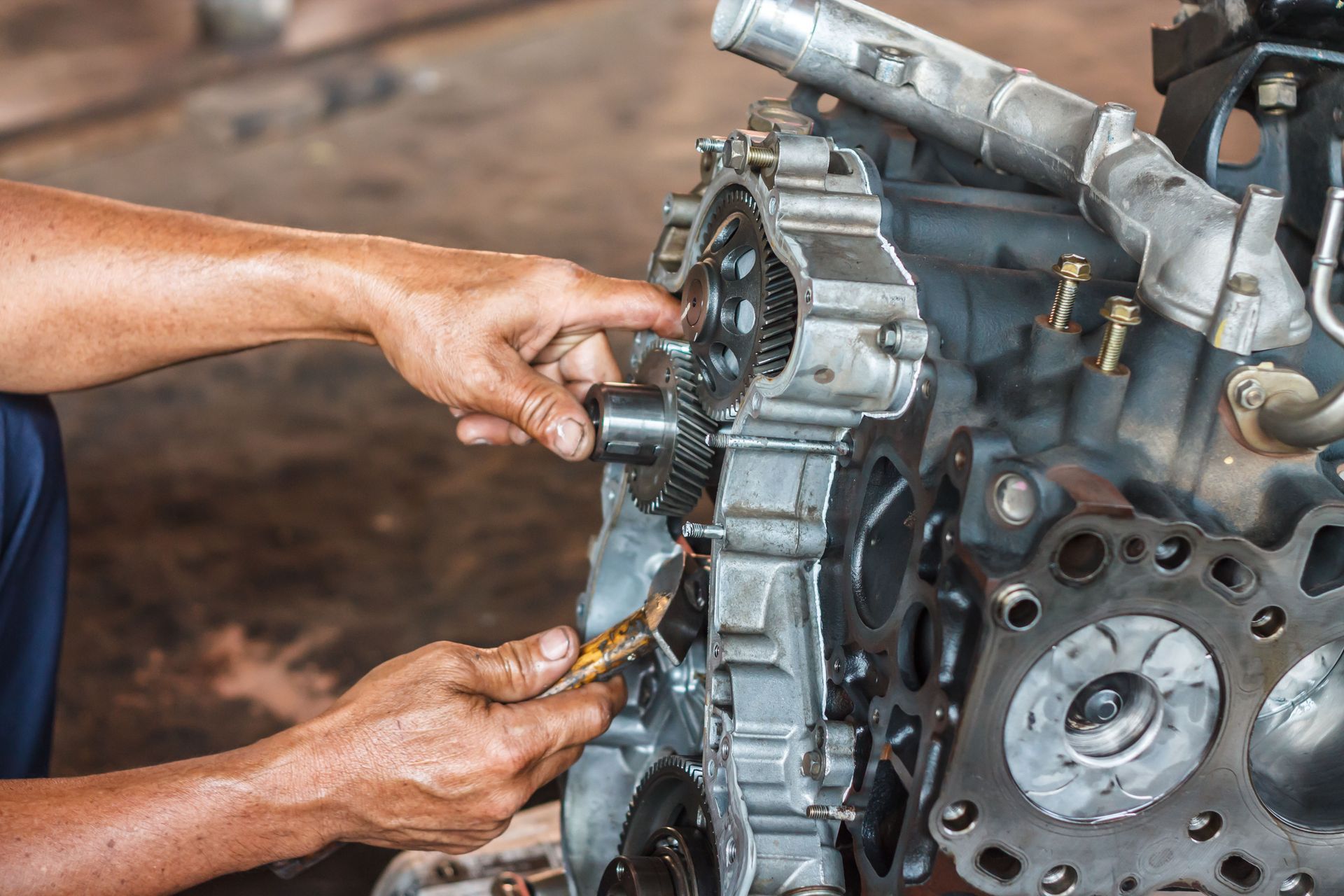 Hands repairing a metallic engine component with tools in a workshop