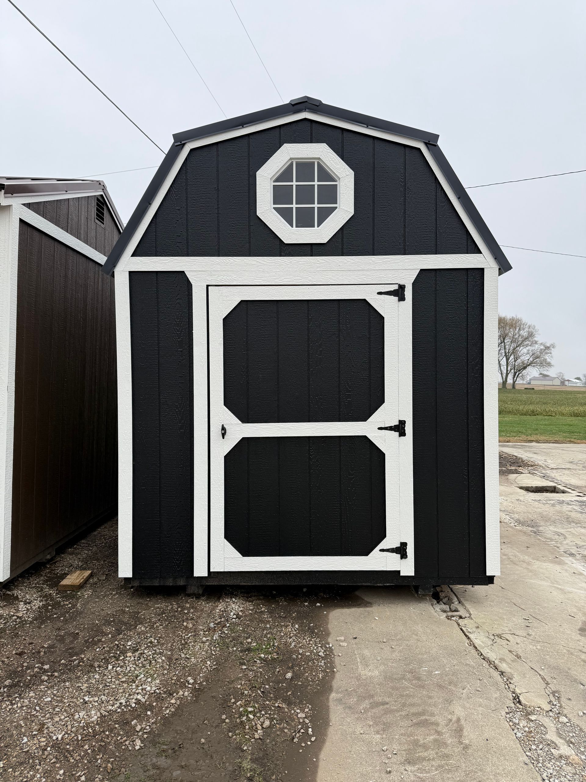 Black and white barn-style shed with an octagonal window above the door.