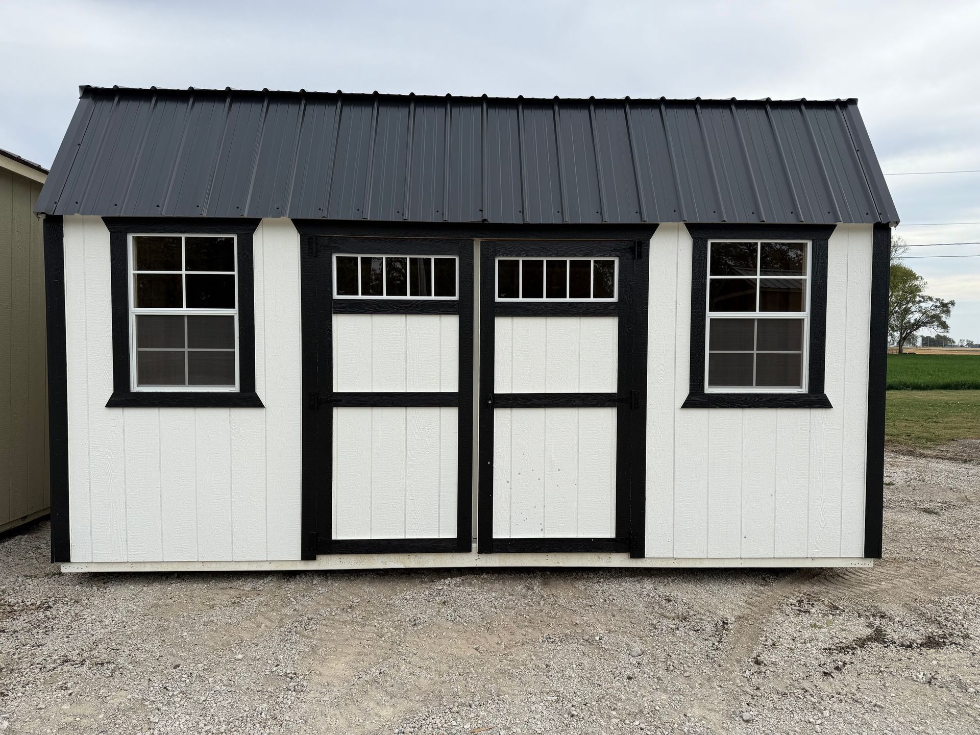 White storage shed with black trim, black roof, and two windows and doors.