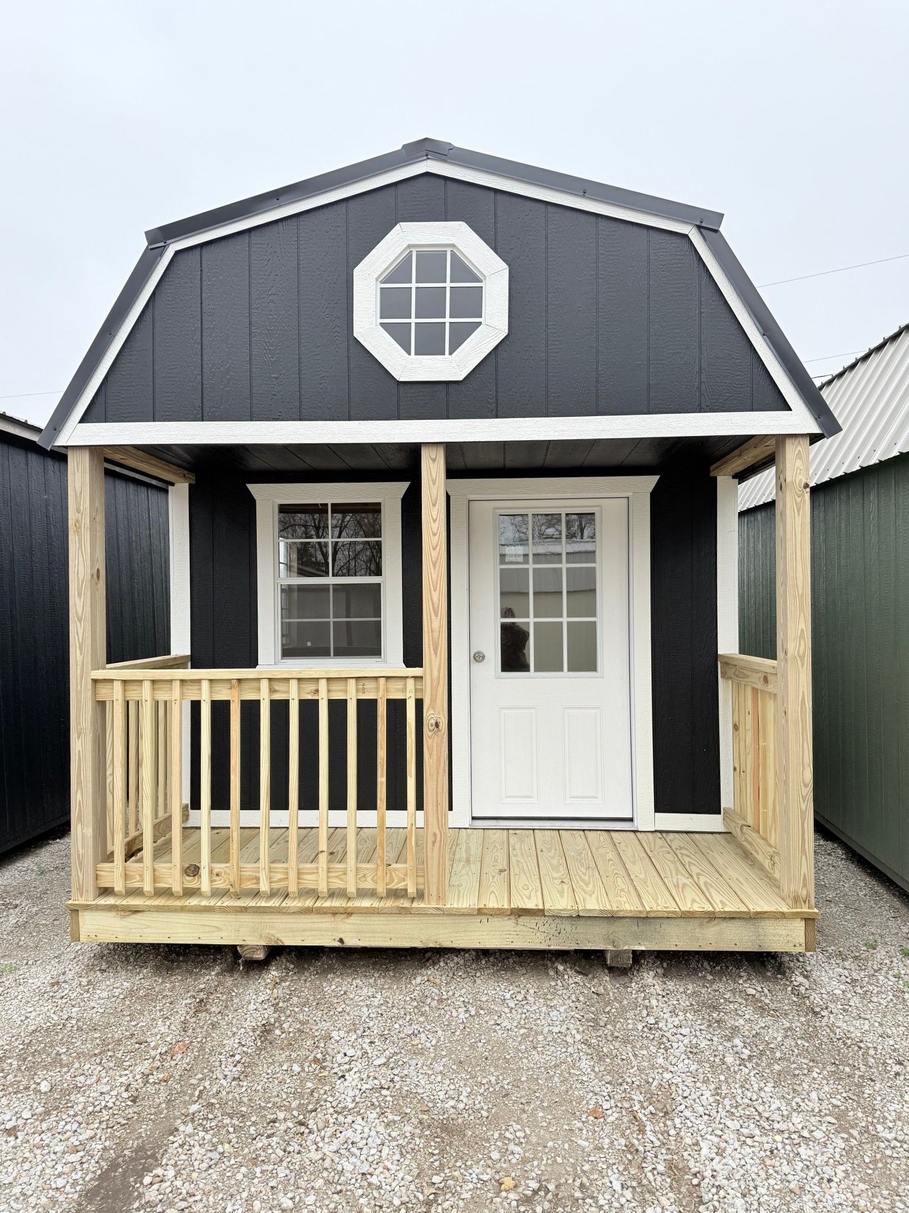 Black and white storage shed with a small porch and white-framed windows.