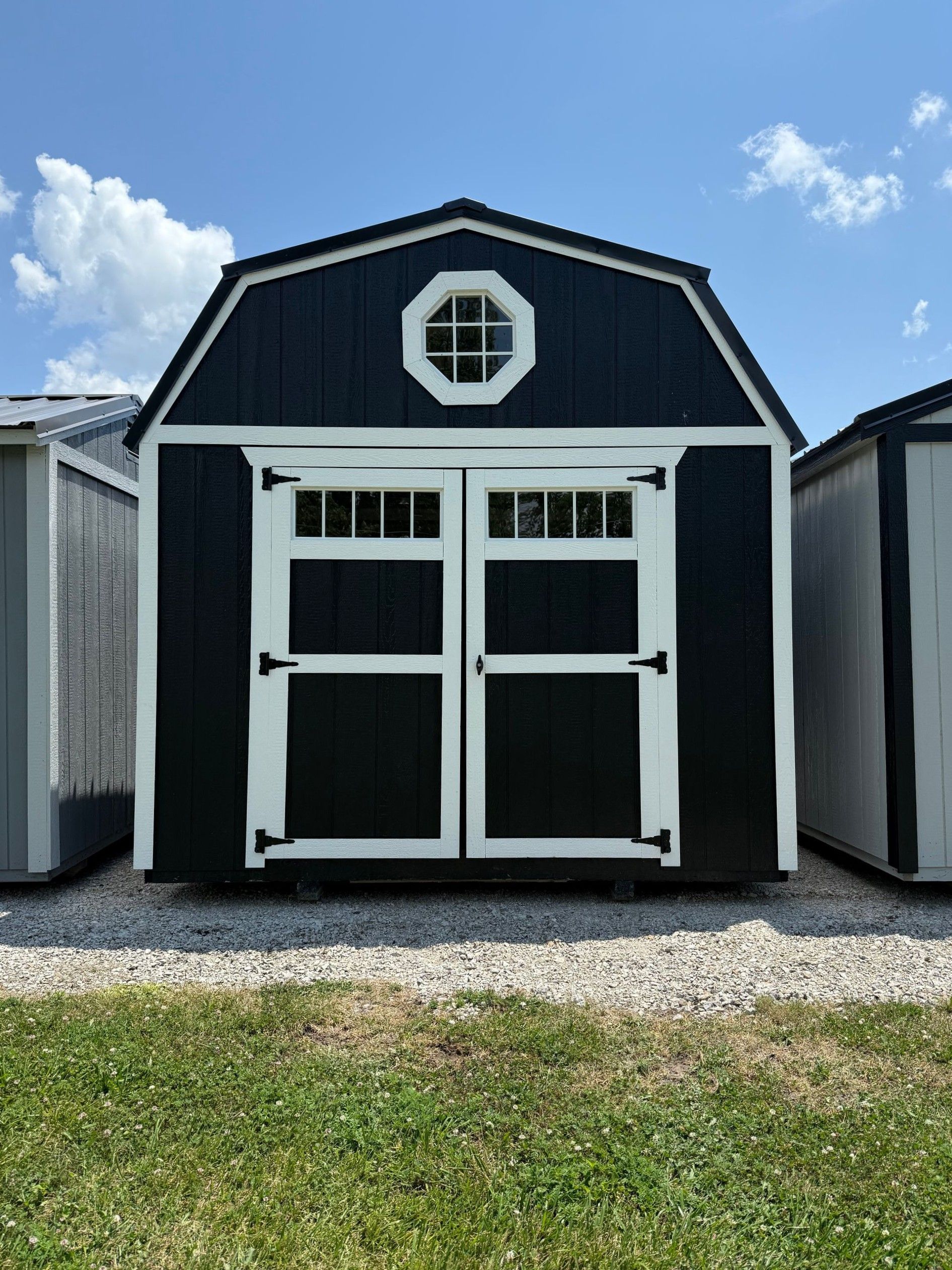Black shed with white trim, double doors, and a round window under a blue sky.