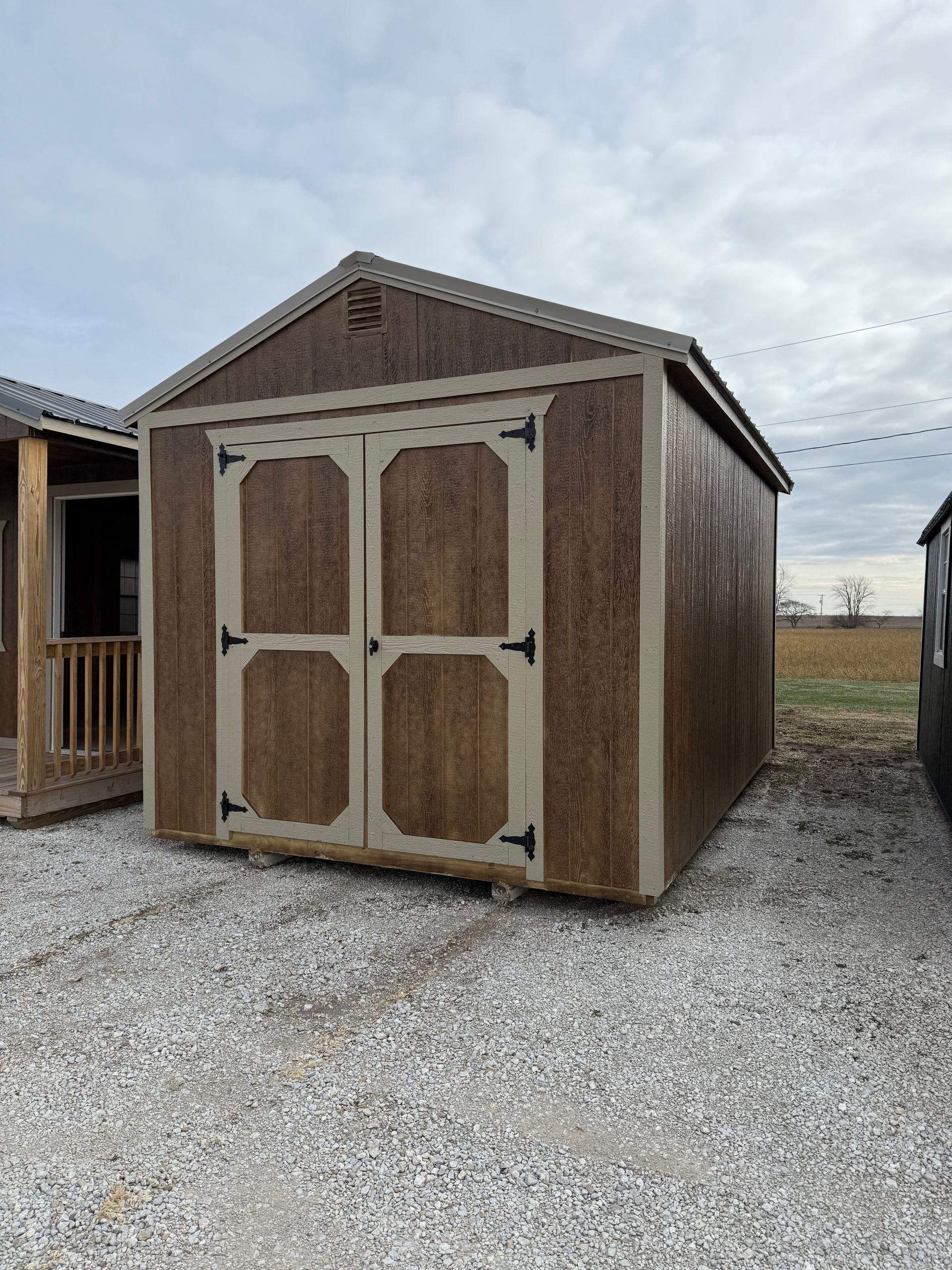 Brown shed with tan trim and double doors on gravel.