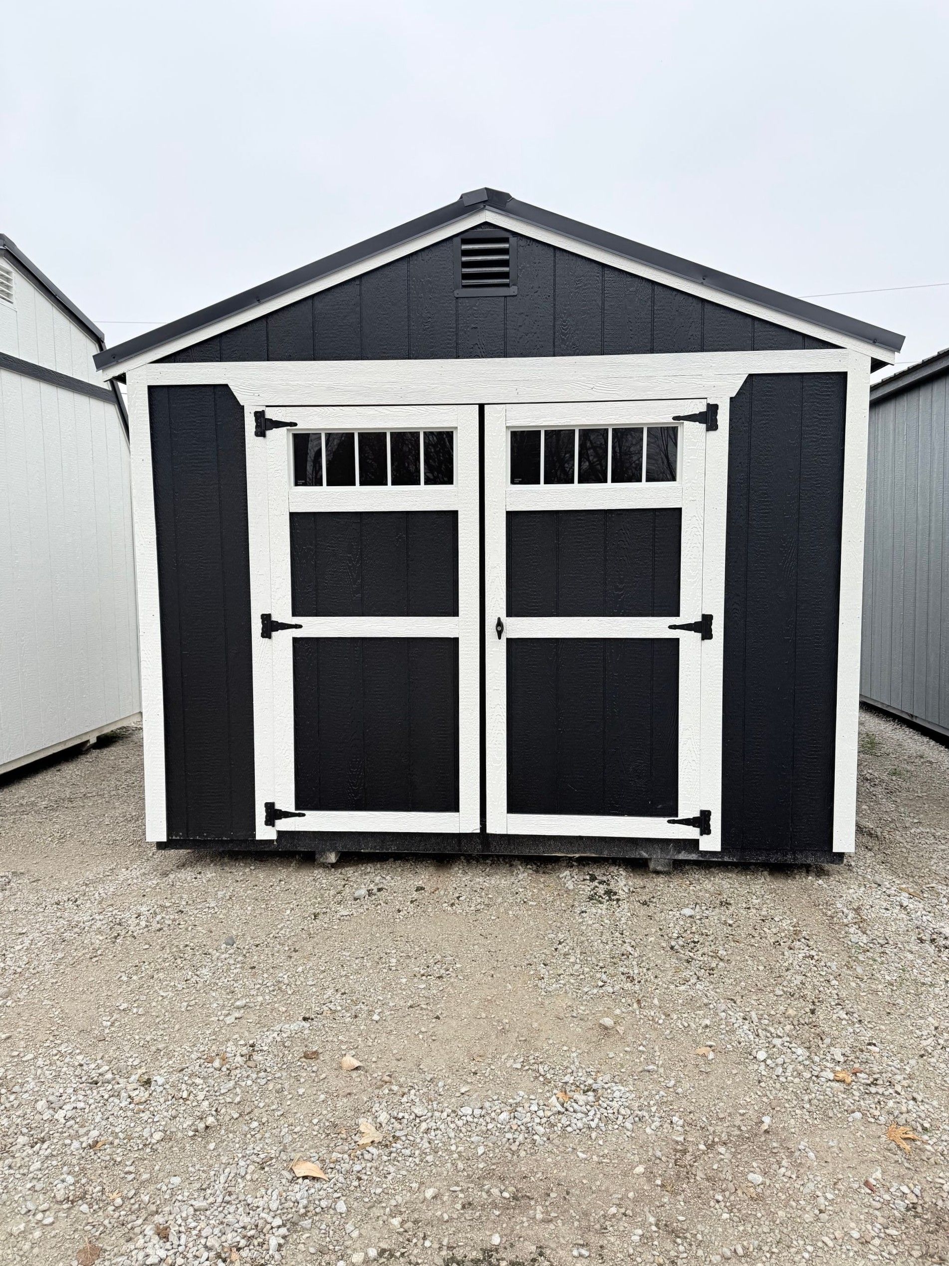 Black shed with white trim and double doors on gravel.