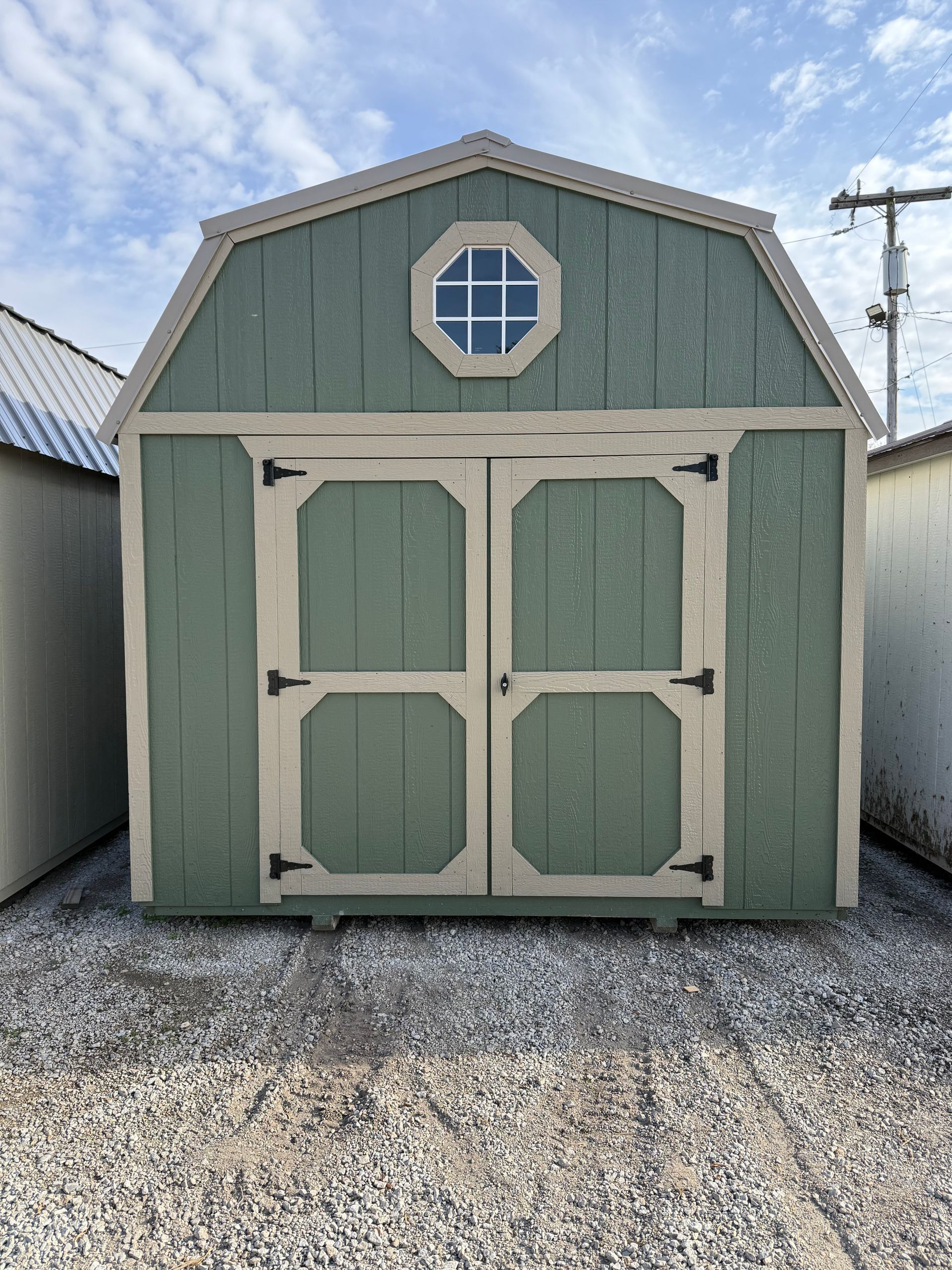 Green barn shed with cream trim, double doors, and an octagonal window.
