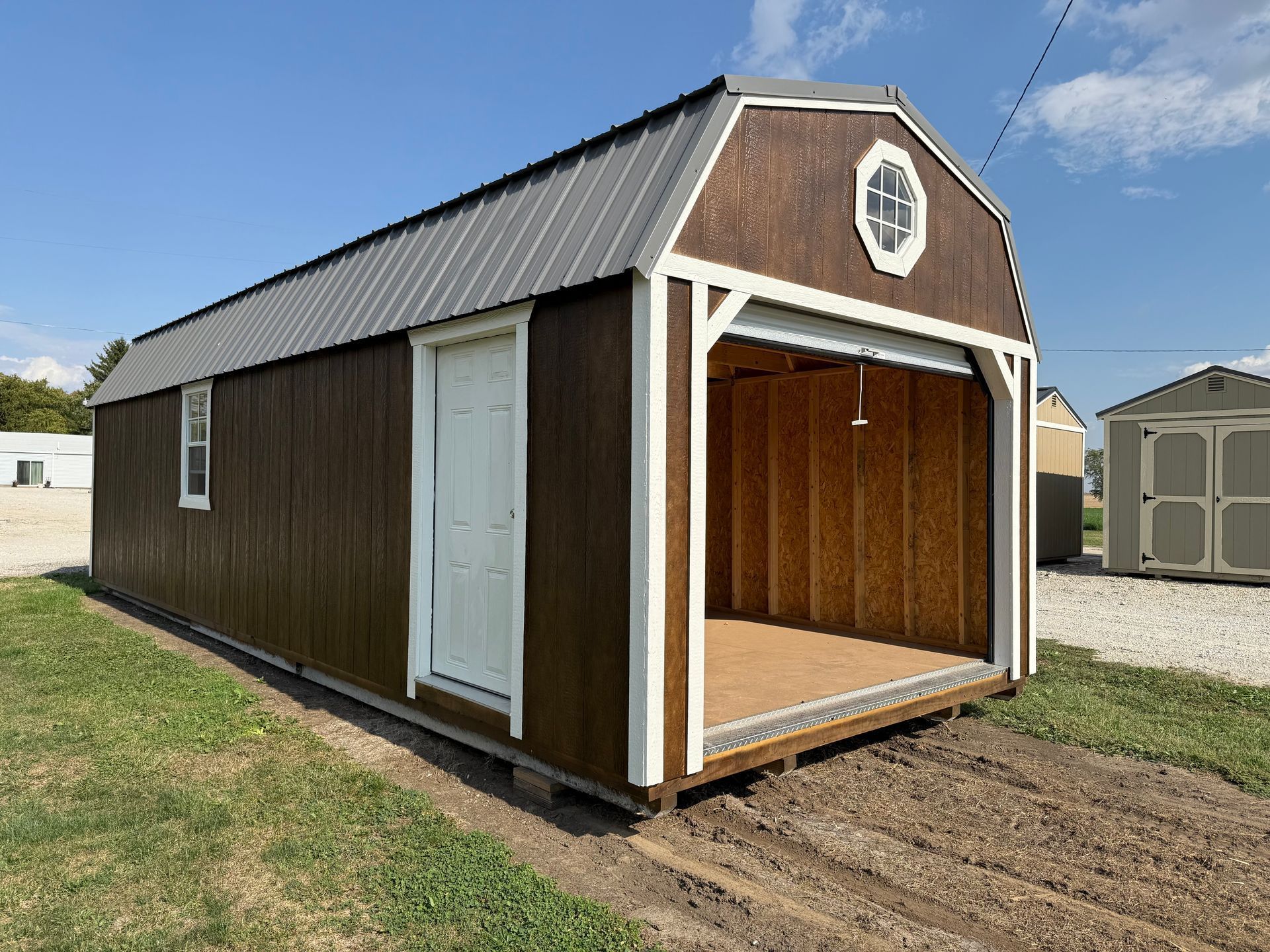 Brown shed with a gray roof and white trim, open garage door, door on the side, on grass.