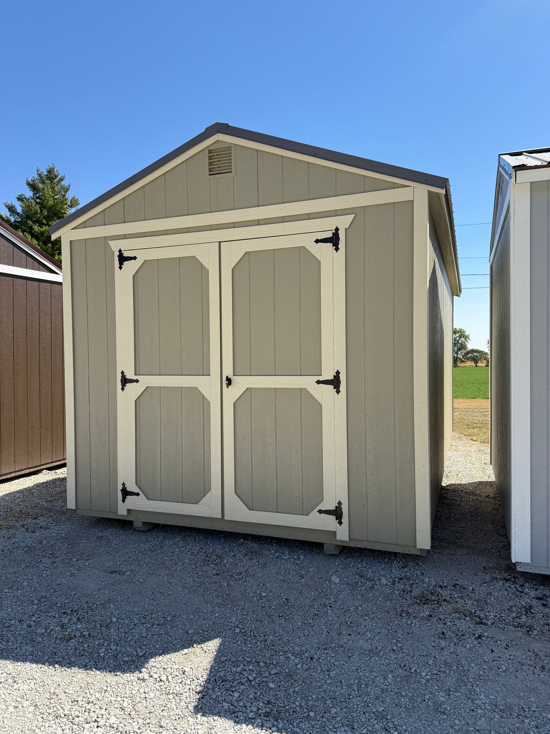 Gray shed with white-trimmed double doors, black hardware, and gray roof, sitting on gravel.