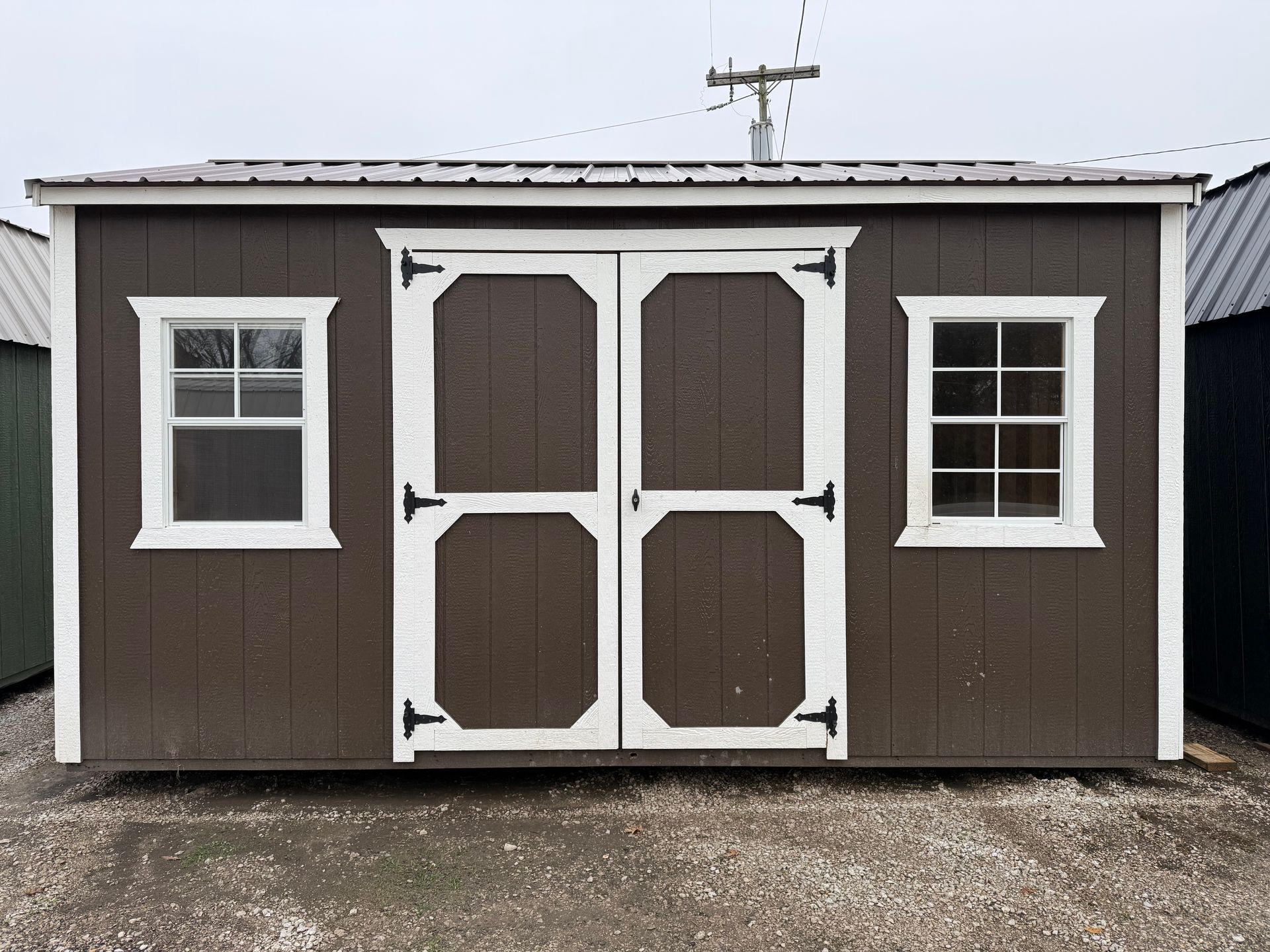 Brown shed with white-trimmed double doors and windows. Gray roof.