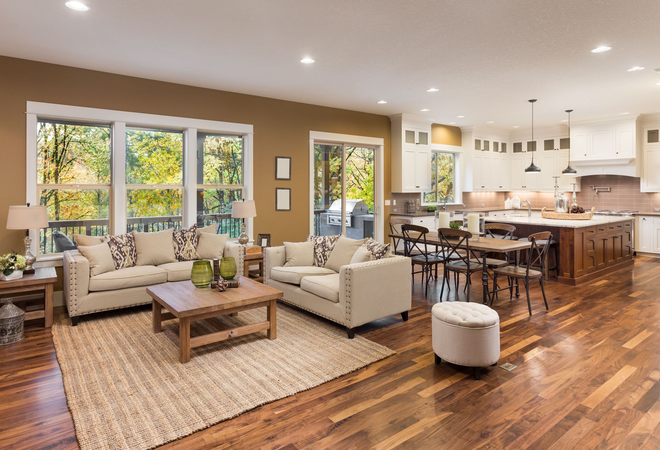 Bright open-plan living room and kitchen with beige sofas, wood floors, large windows, and a dining area 