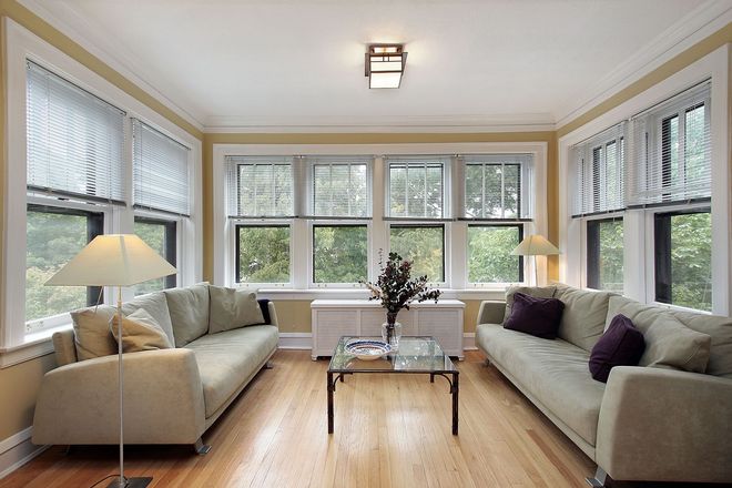 Bright sunroom with two cream sofas, large windows, hardwood floor, and a small coffee table