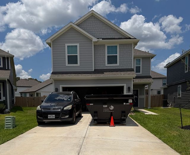 Suburban house with two cars parked in the driveway and a black dumpster by the garage.