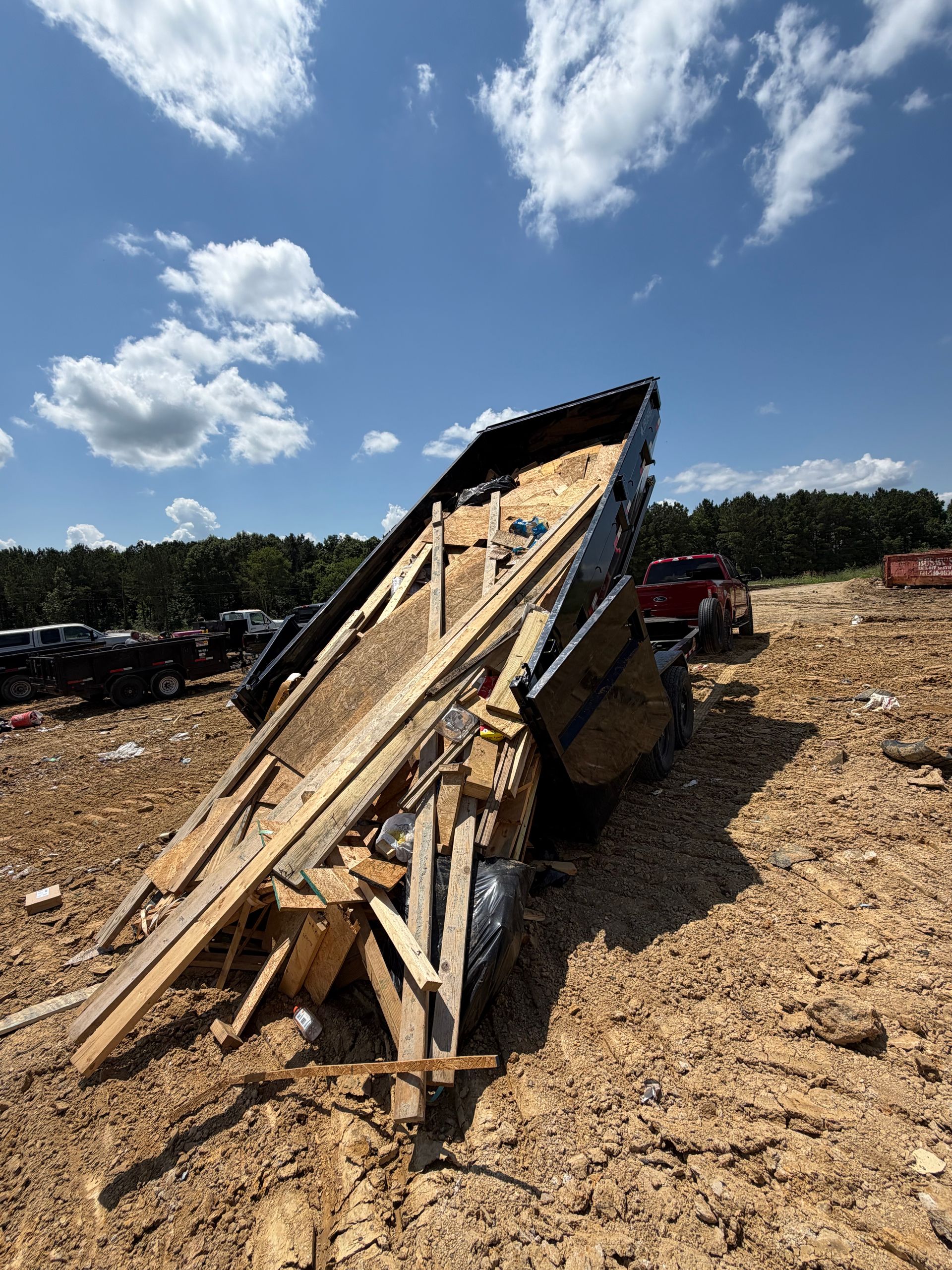 Broken wooden structure tipped over on a dirt field under a blue sky with clouds.