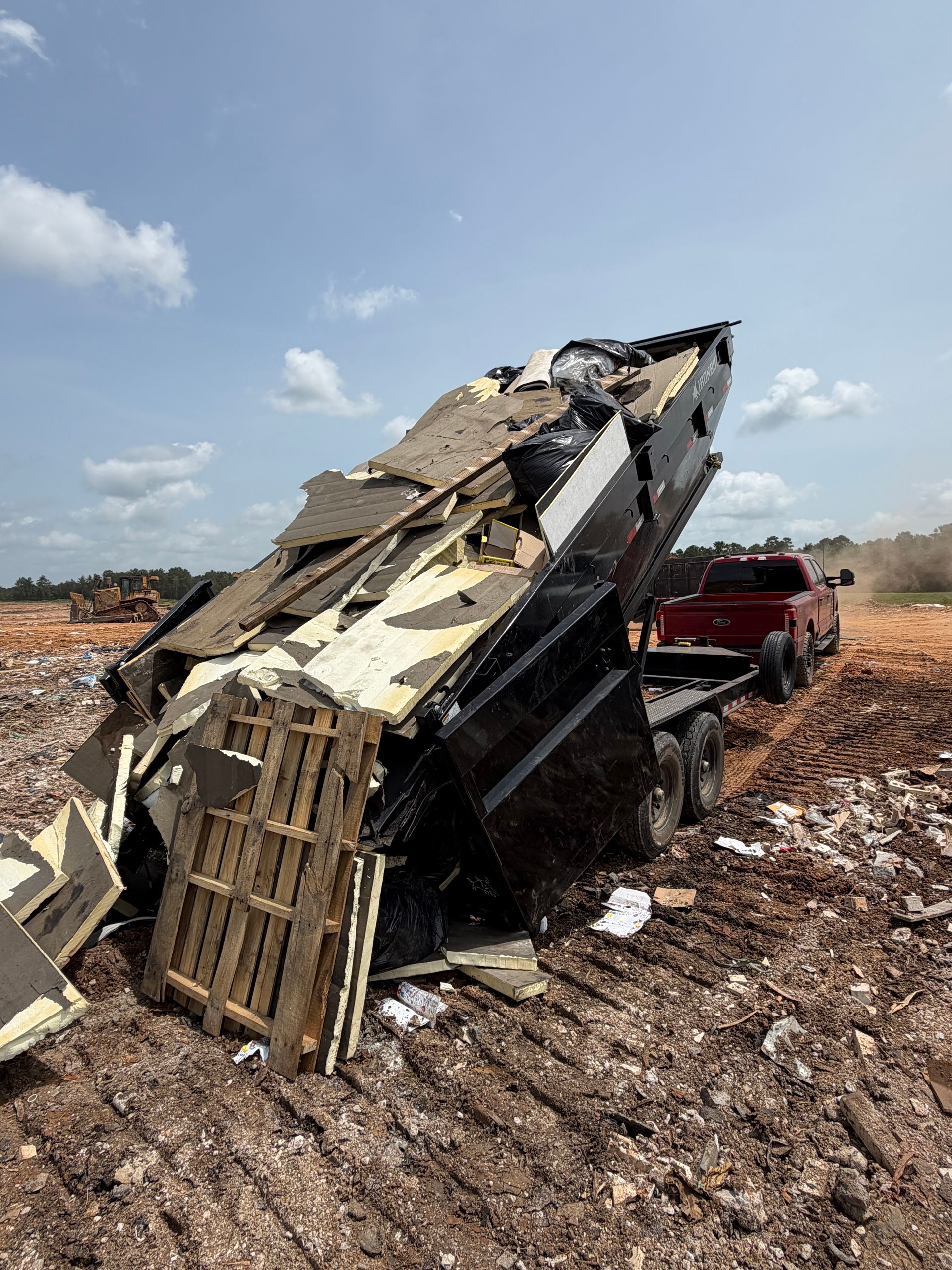 Overturned dump truck in a dirt field with debris scattered around and a red pickup nearby