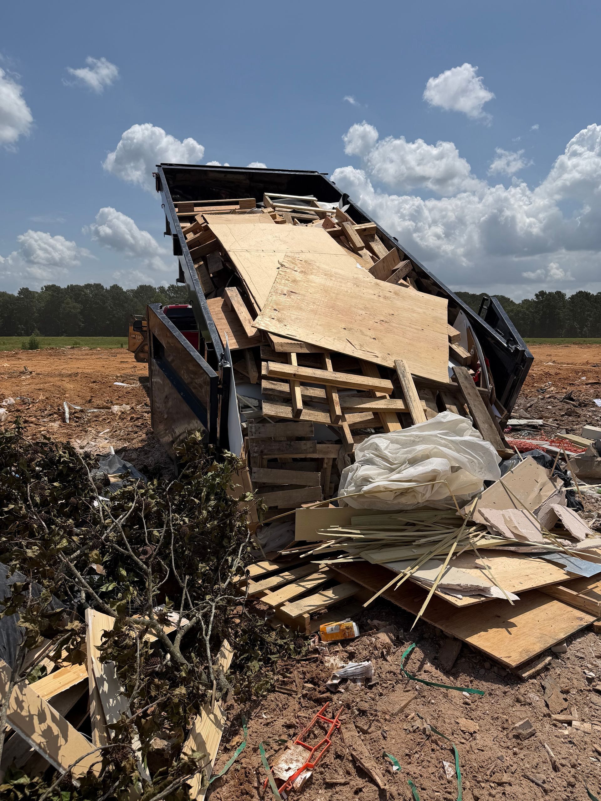 Damaged truck bed loaded with debris in a field under a cloudy sky