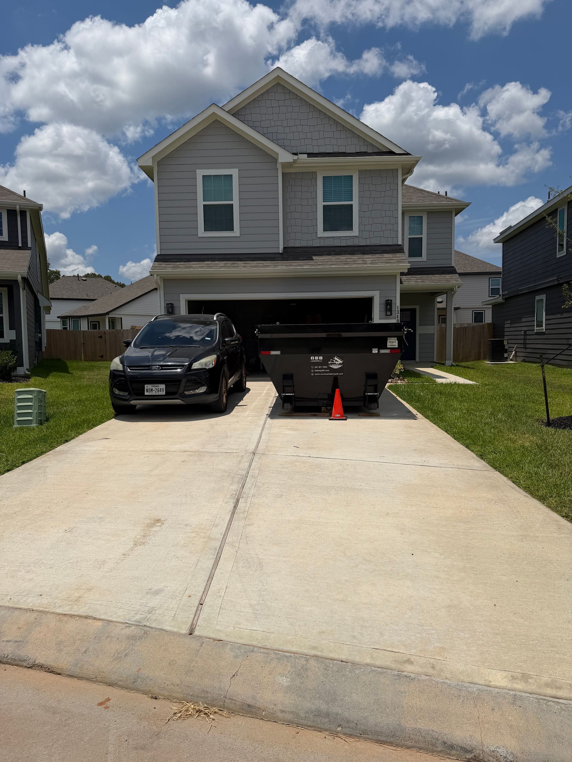 Two-story gray house with a steep driveway, black SUV parked in front, and orange cones by the garage.