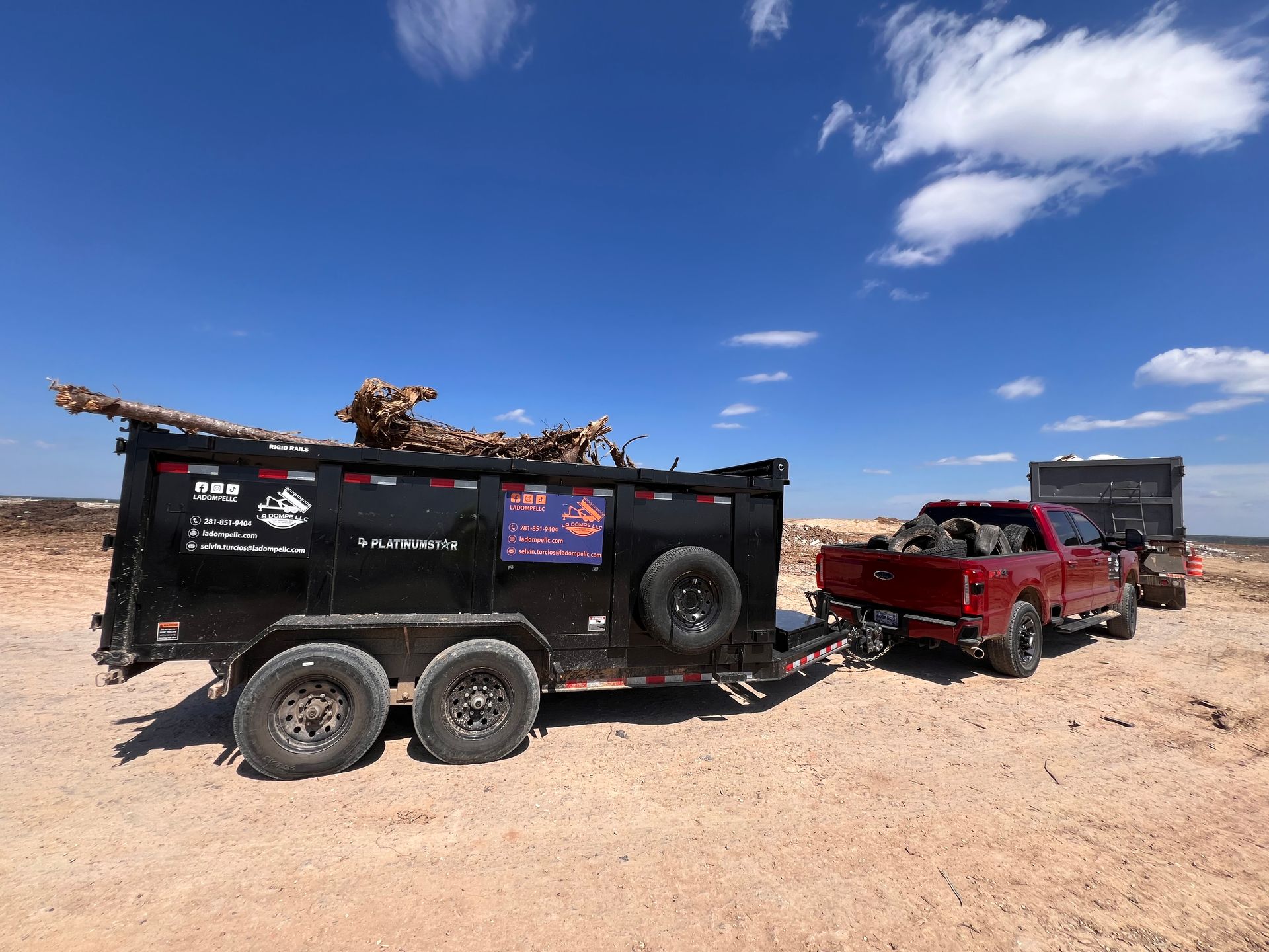 Red pickup truck towing a black off-road trailer in a sandy desert under a blue sky