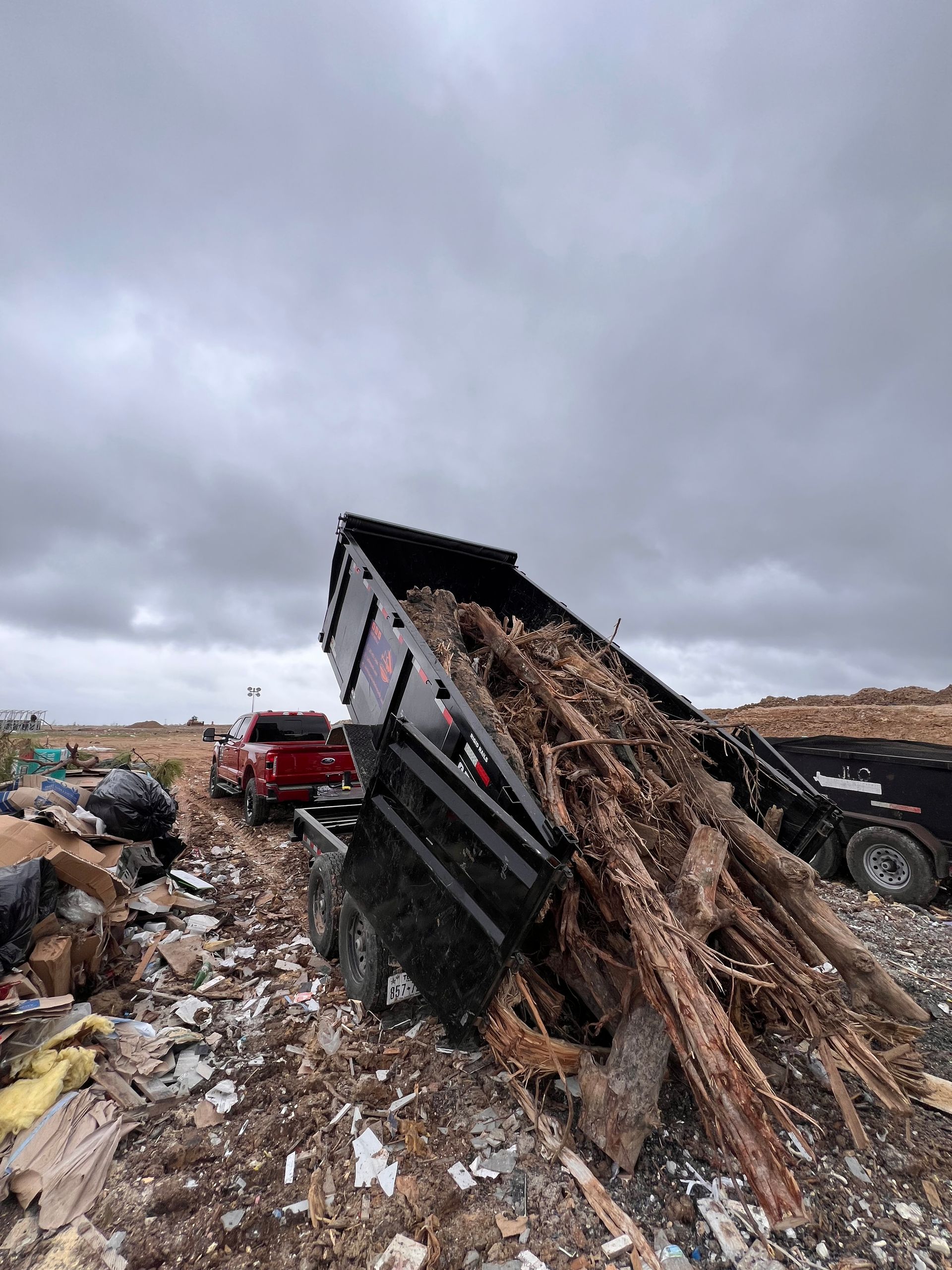 Overturned dump truck loaded with debris on muddy roadside under cloudy sky