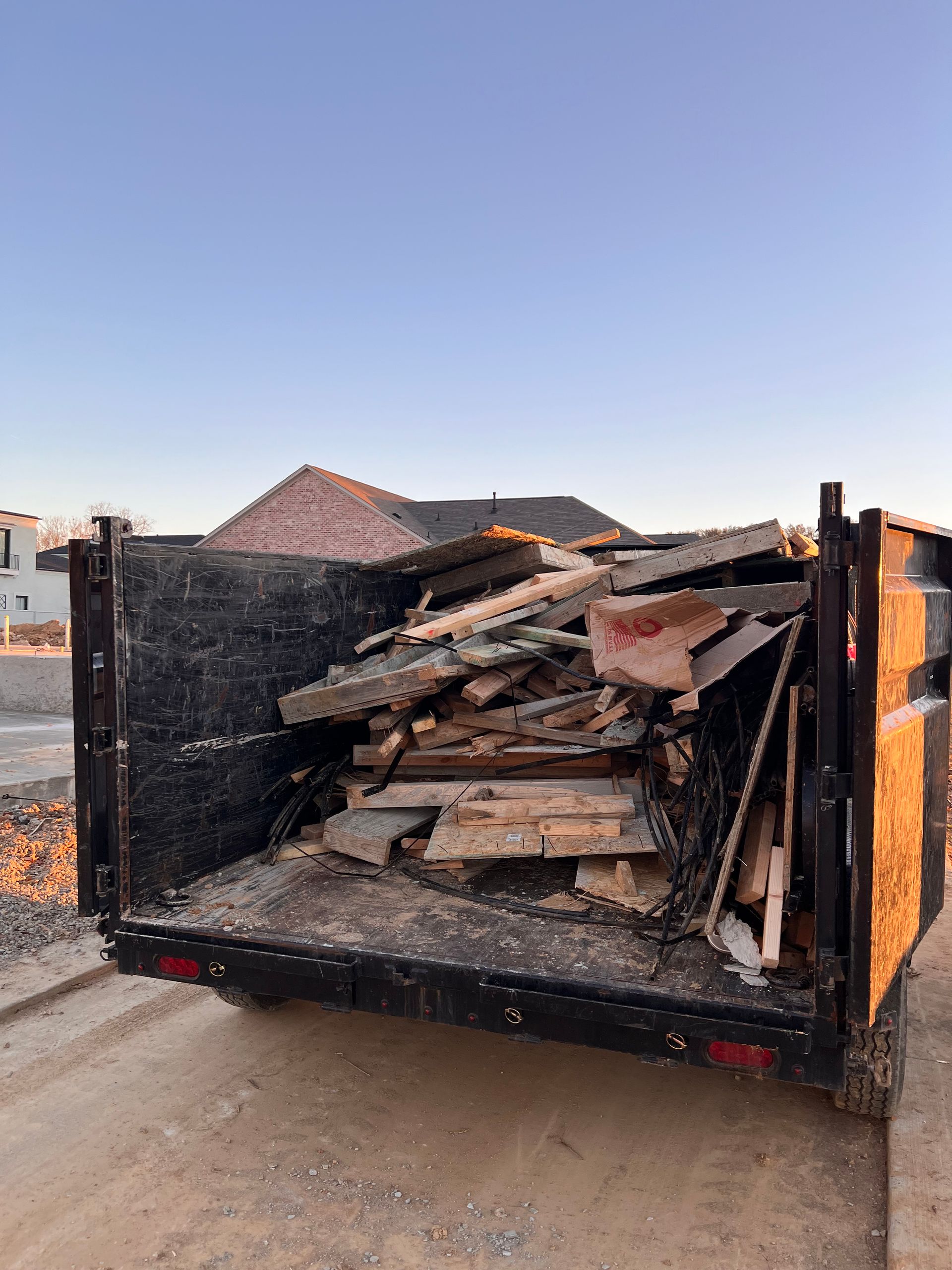 Dump trailer loaded with broken wood and debris on a dirt road at sunset