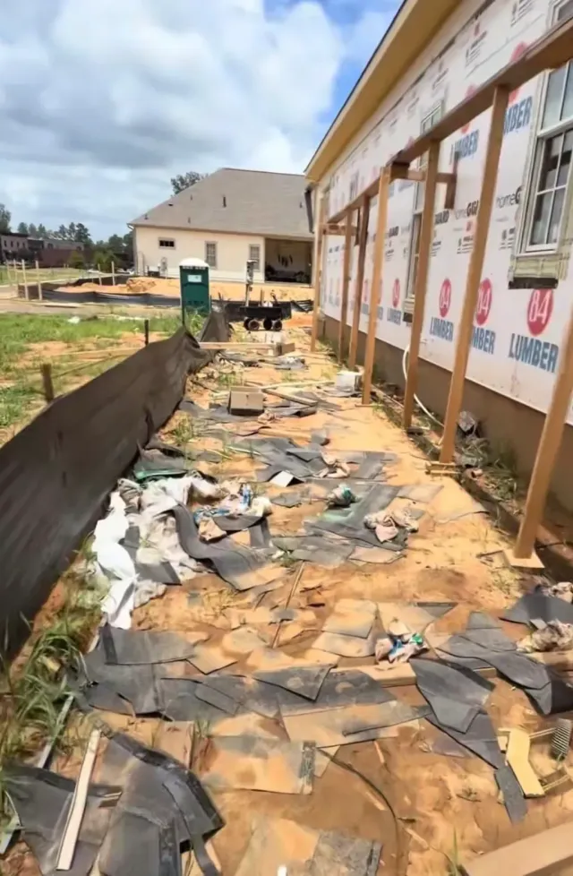 Debris-strewn walkway beside a school building, with damaged roofing and scattered trash along the wall.