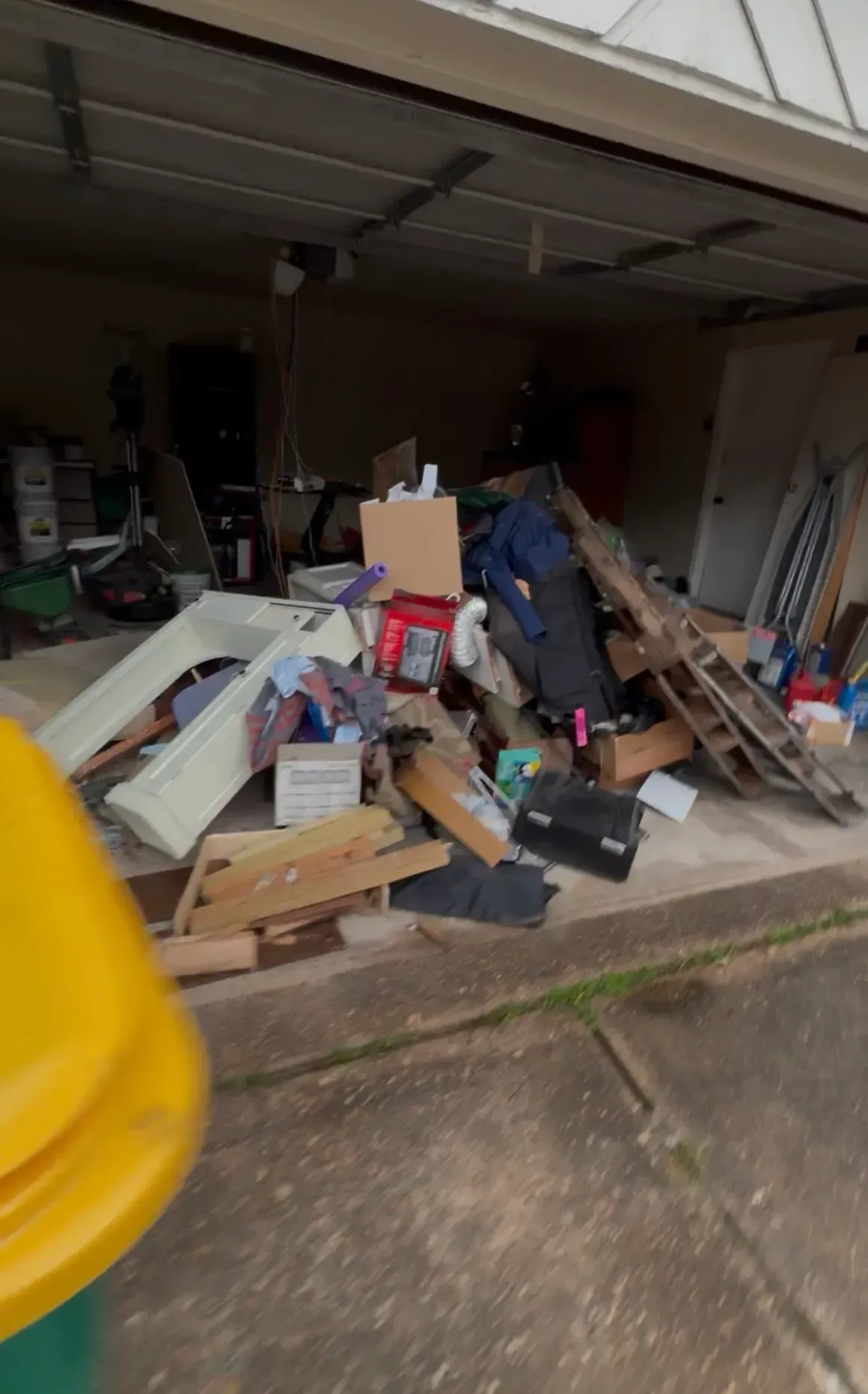 Garage cluttered with piled scrap wood, tools, and debris under an open door
