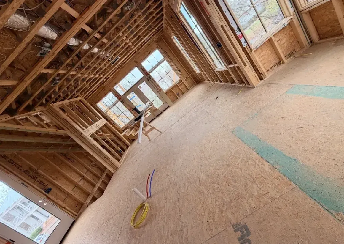 Unfinished room with exposed wood framing, windows, and a broom on the plywood floor.