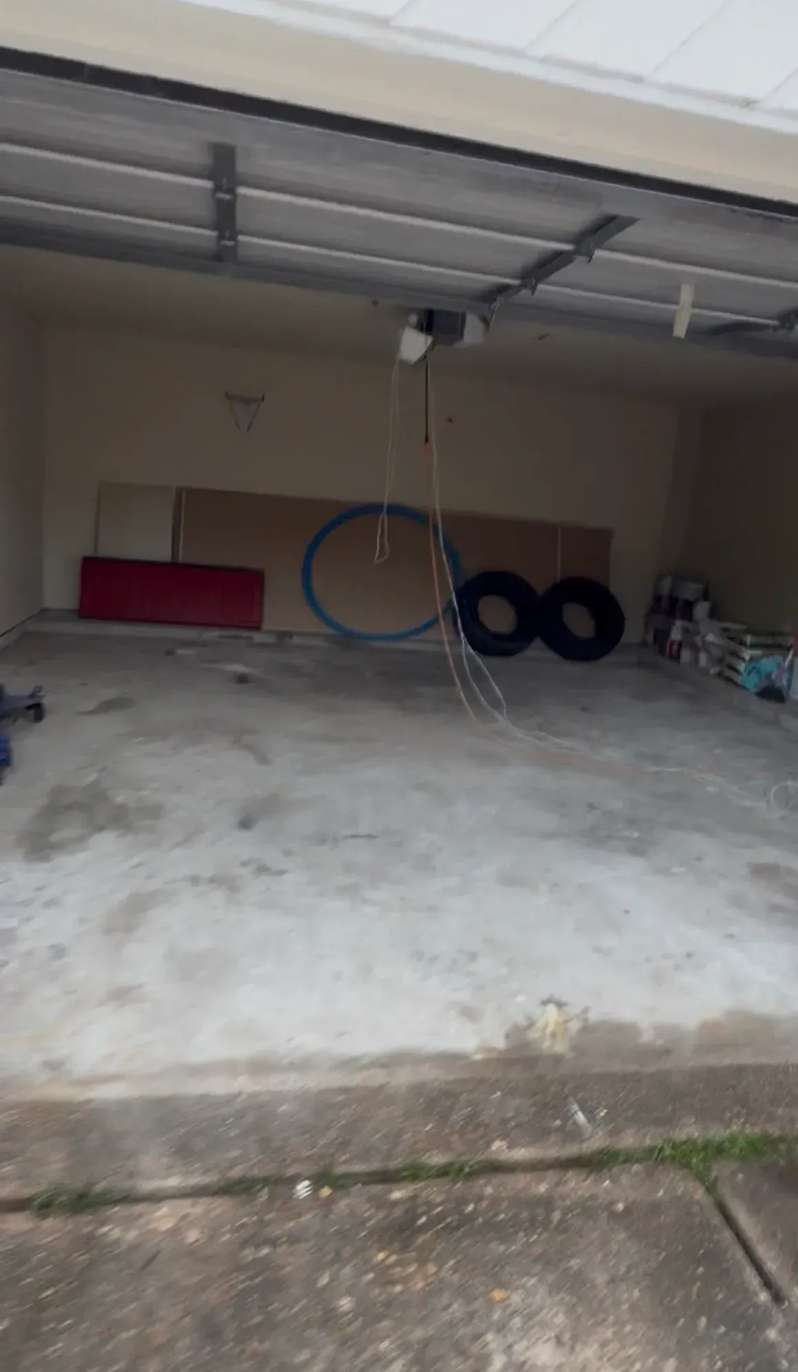 Empty garage with concrete floor, red storage bin, hanging blue hose, and stacked tires near the back wall