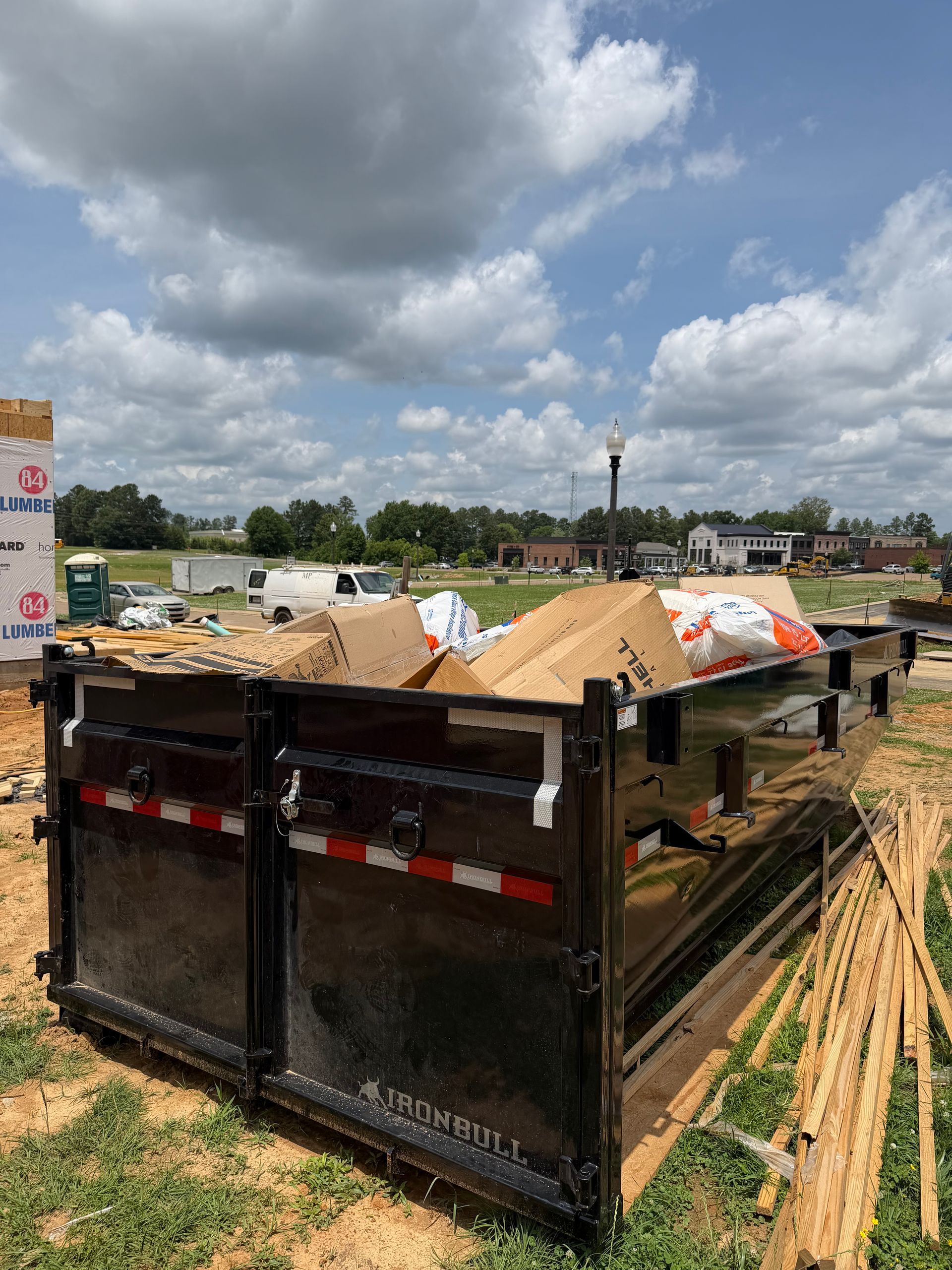 A black dump trailer loaded with sand at a construction site under a cloudy sky.