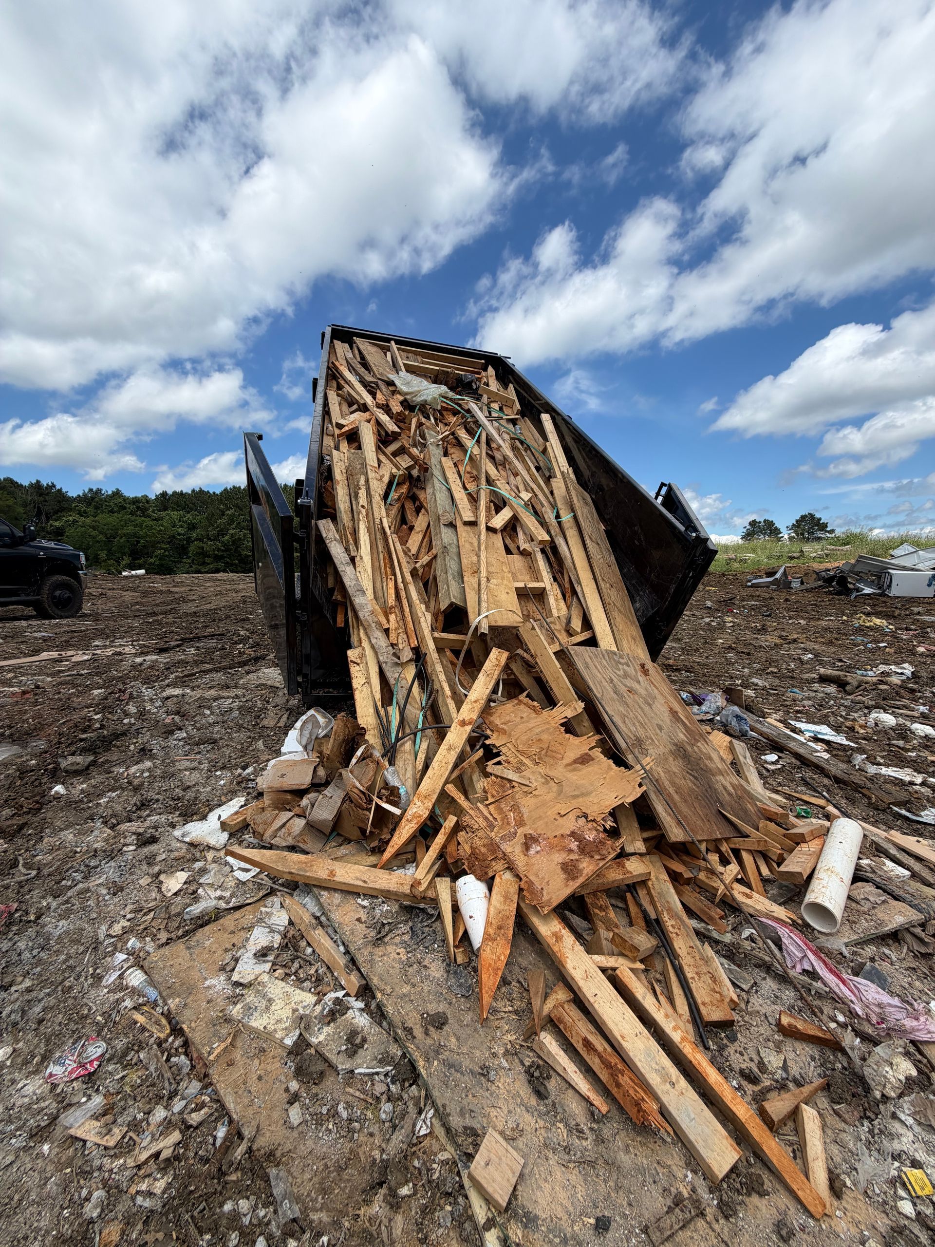 Collapsed wooden structure in a muddy field under a cloudy blue sky