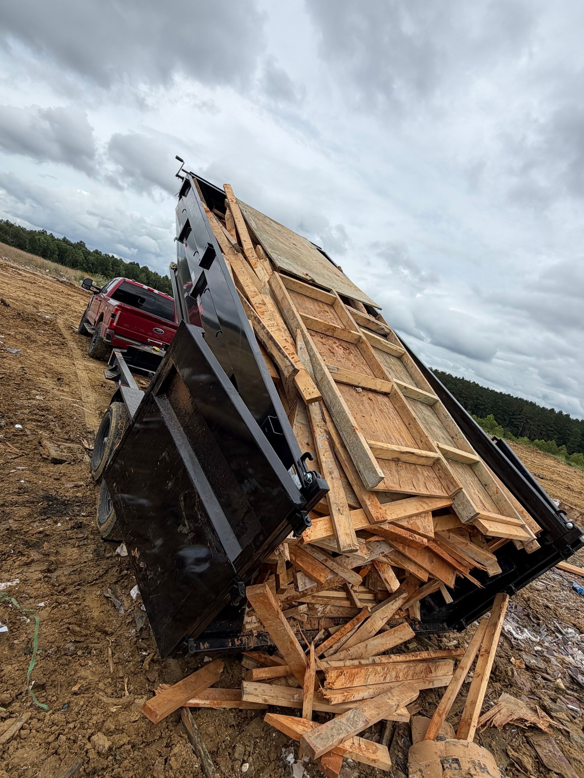 Overturned truck trailer spilling lumber on a dirt road under cloudy sky