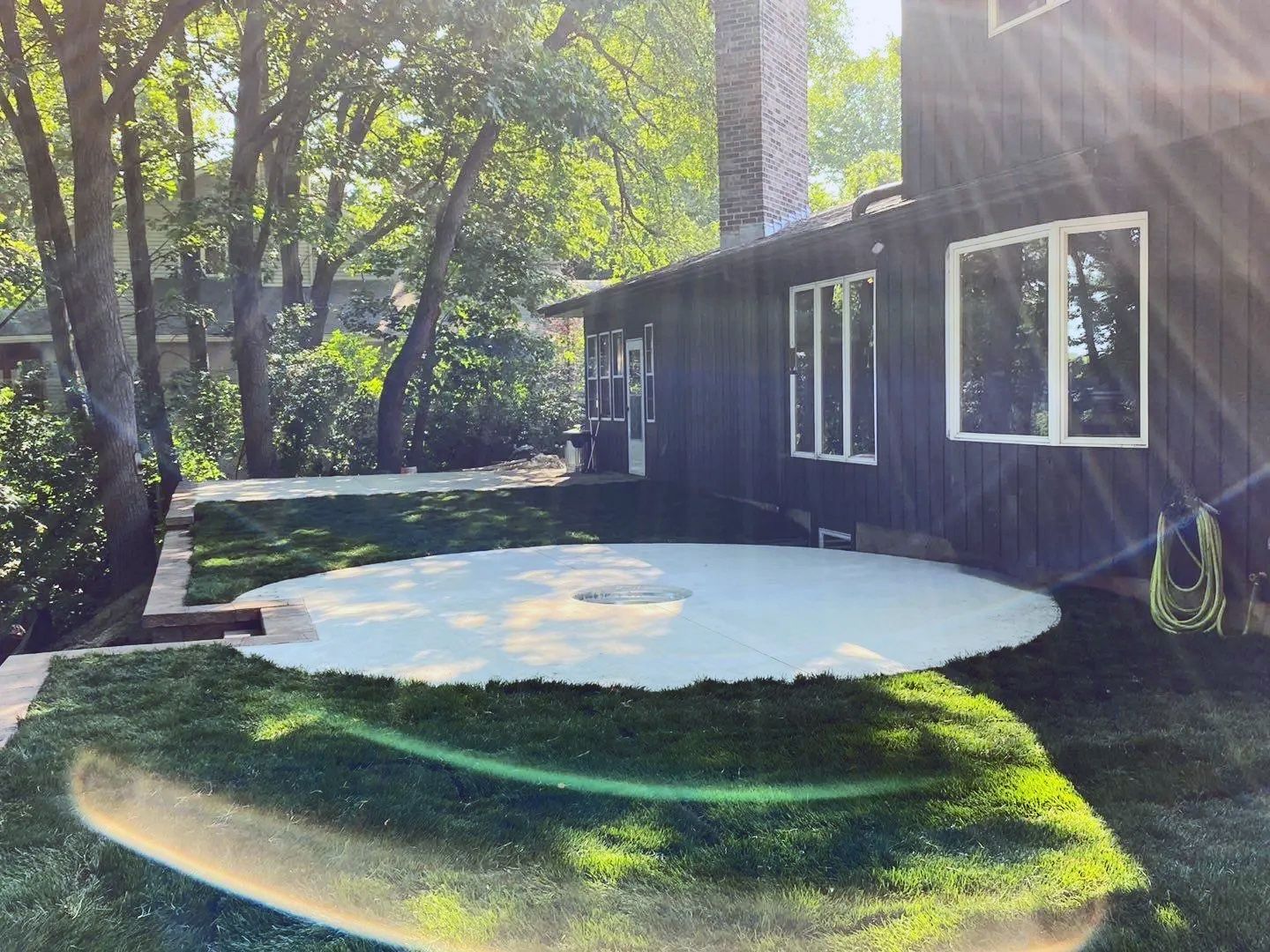 A house with a large, round patio on a grassy lawn with trees in the background.