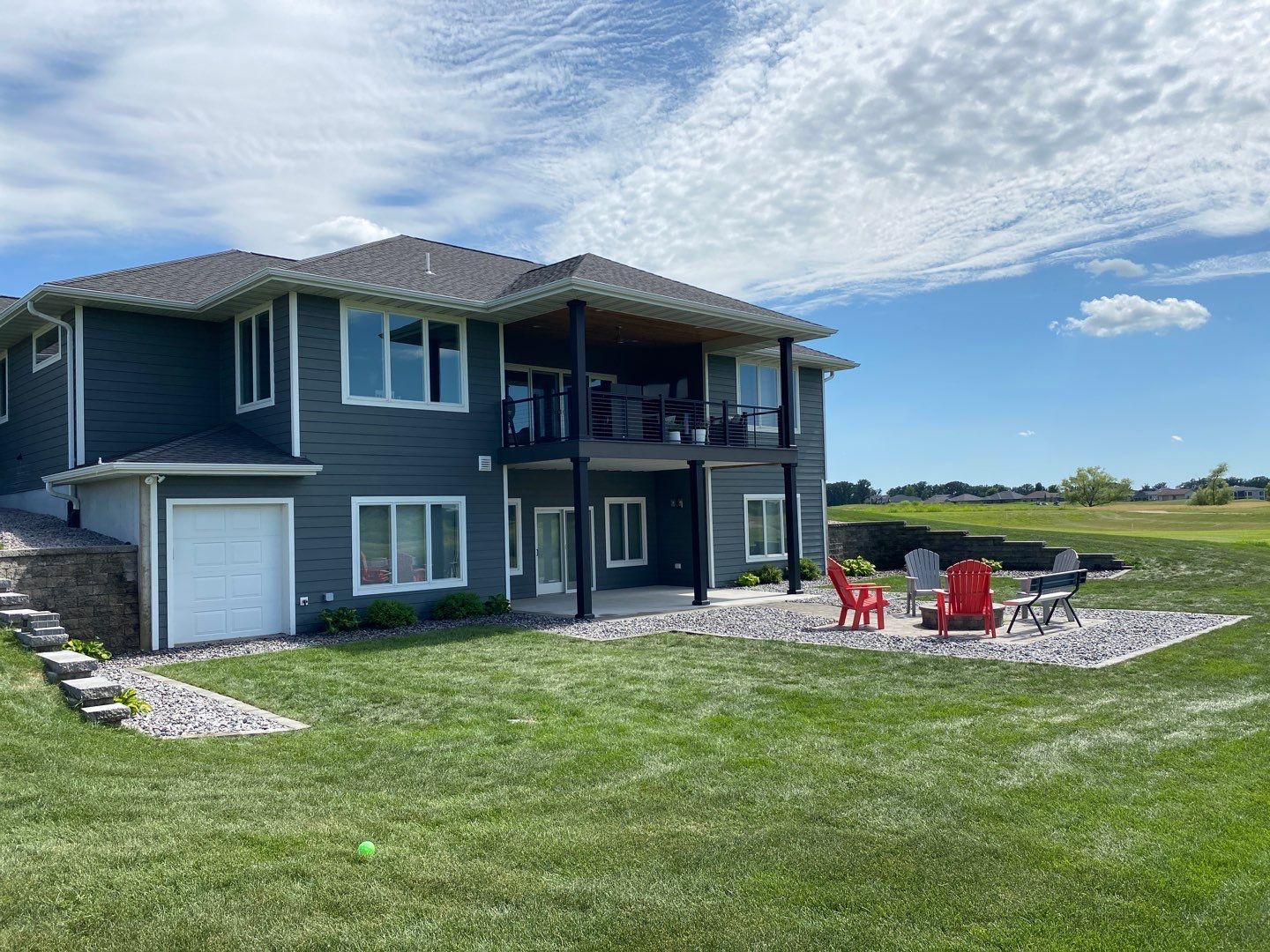 Back of a two-story home with a patio, lawn, and fire pit on a sunny day.