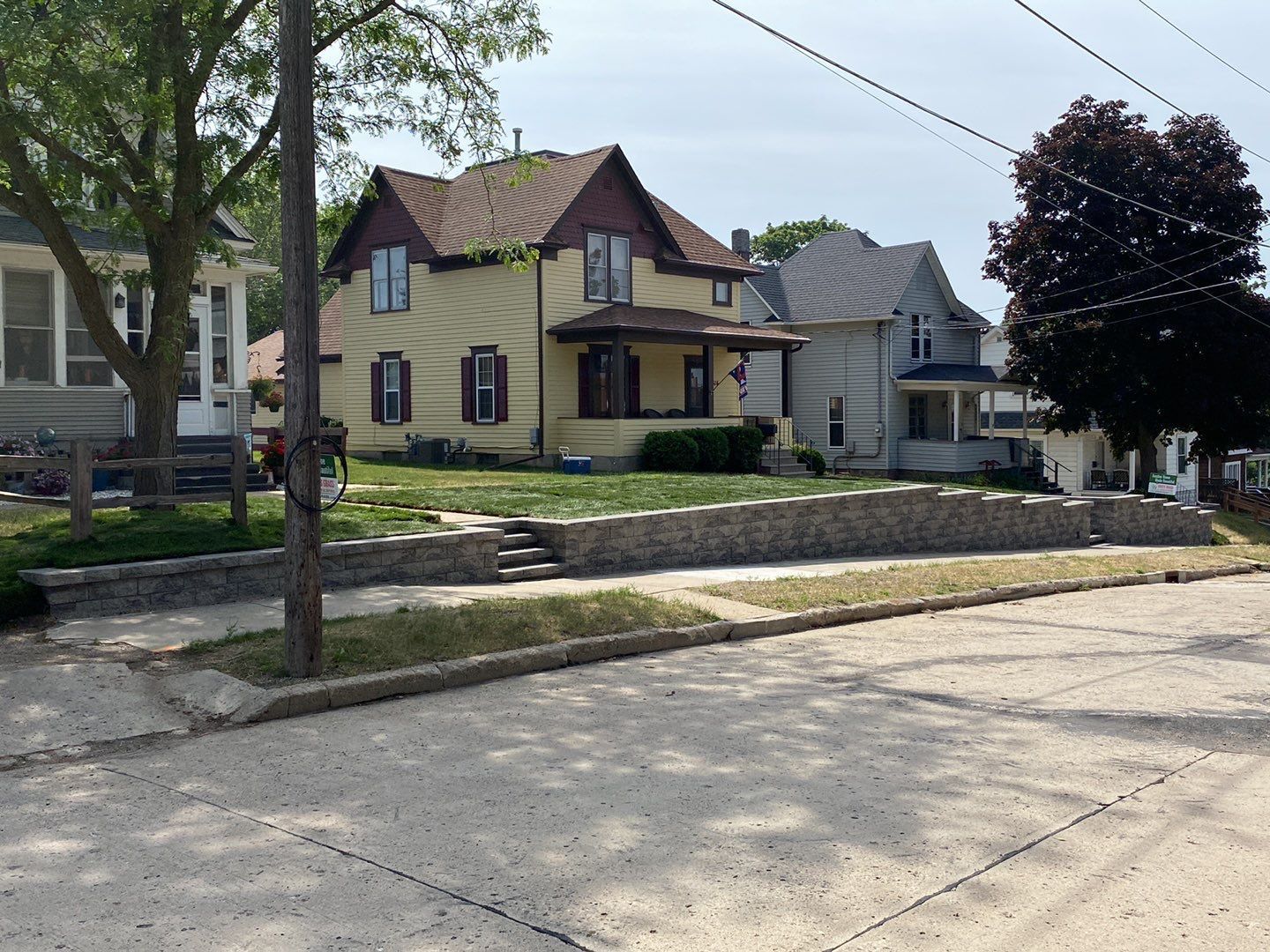 Houses on a residential street. Yellow house with brown roof and porch stands out.