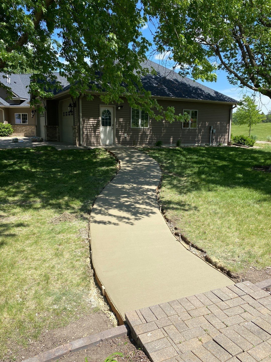Concrete walkway leading to a house with a white door, surrounded by grass and trees.