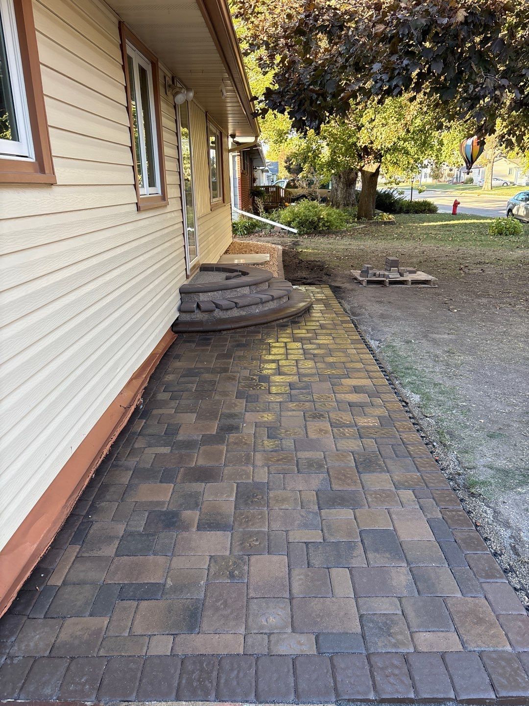 Brick paver walkway beside a beige house with brown trim and steps.