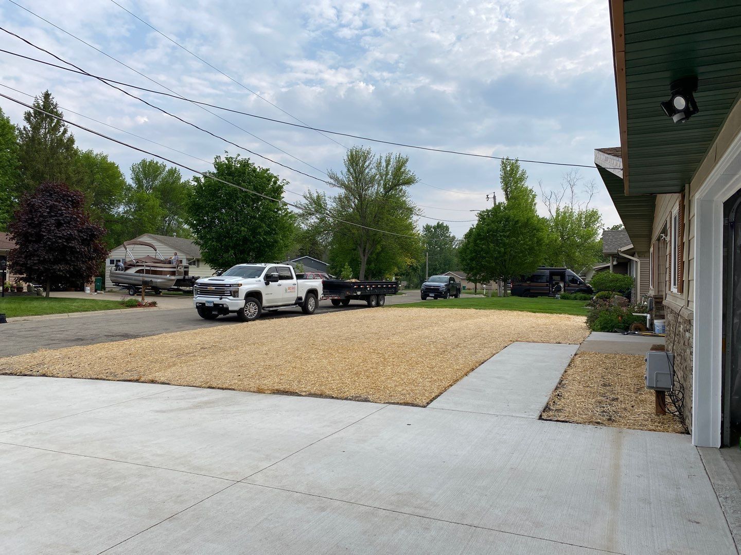 A gravel-covered yard next to a concrete driveway. A white truck and trailer sit on the gravel.