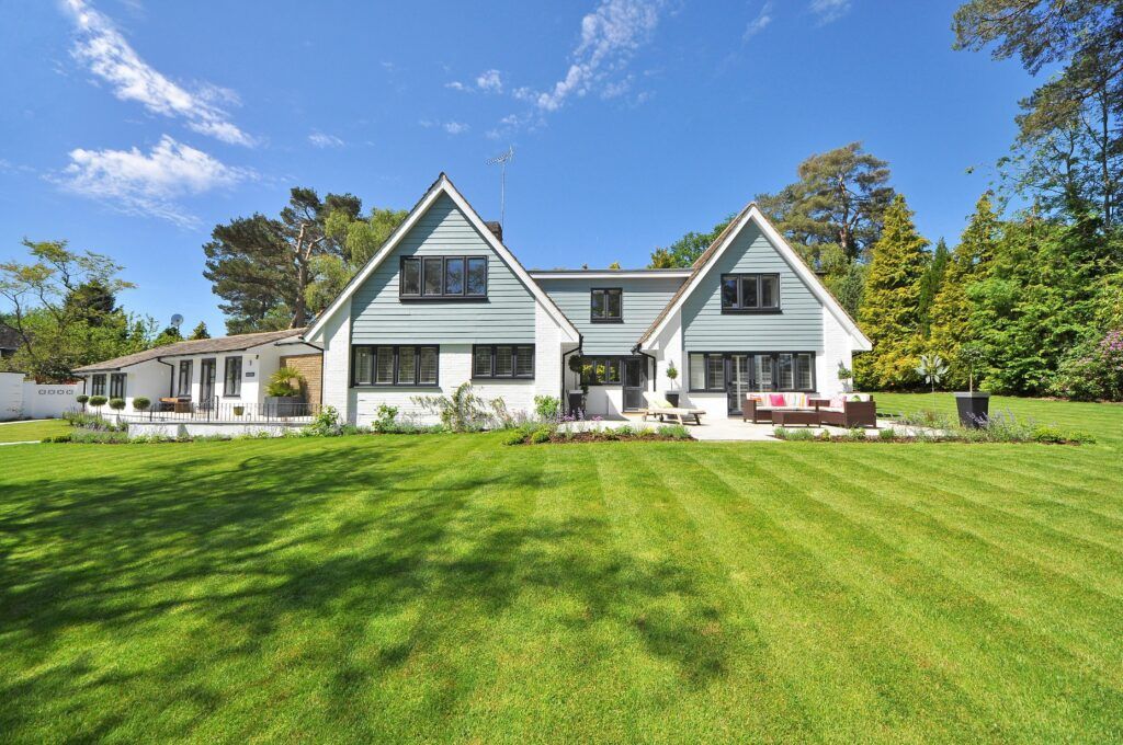 Two-story house with light blue gable, white siding, and black windows, in a green lawn, on a sunny day.