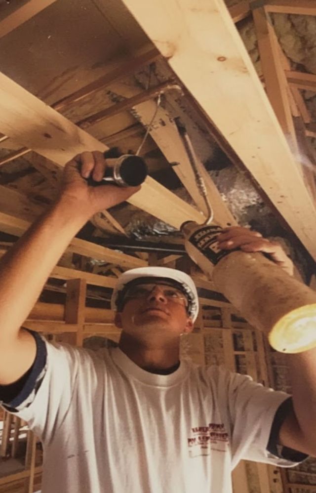 Worker in hard hat using a drill to install ceiling framing in a wooden structure