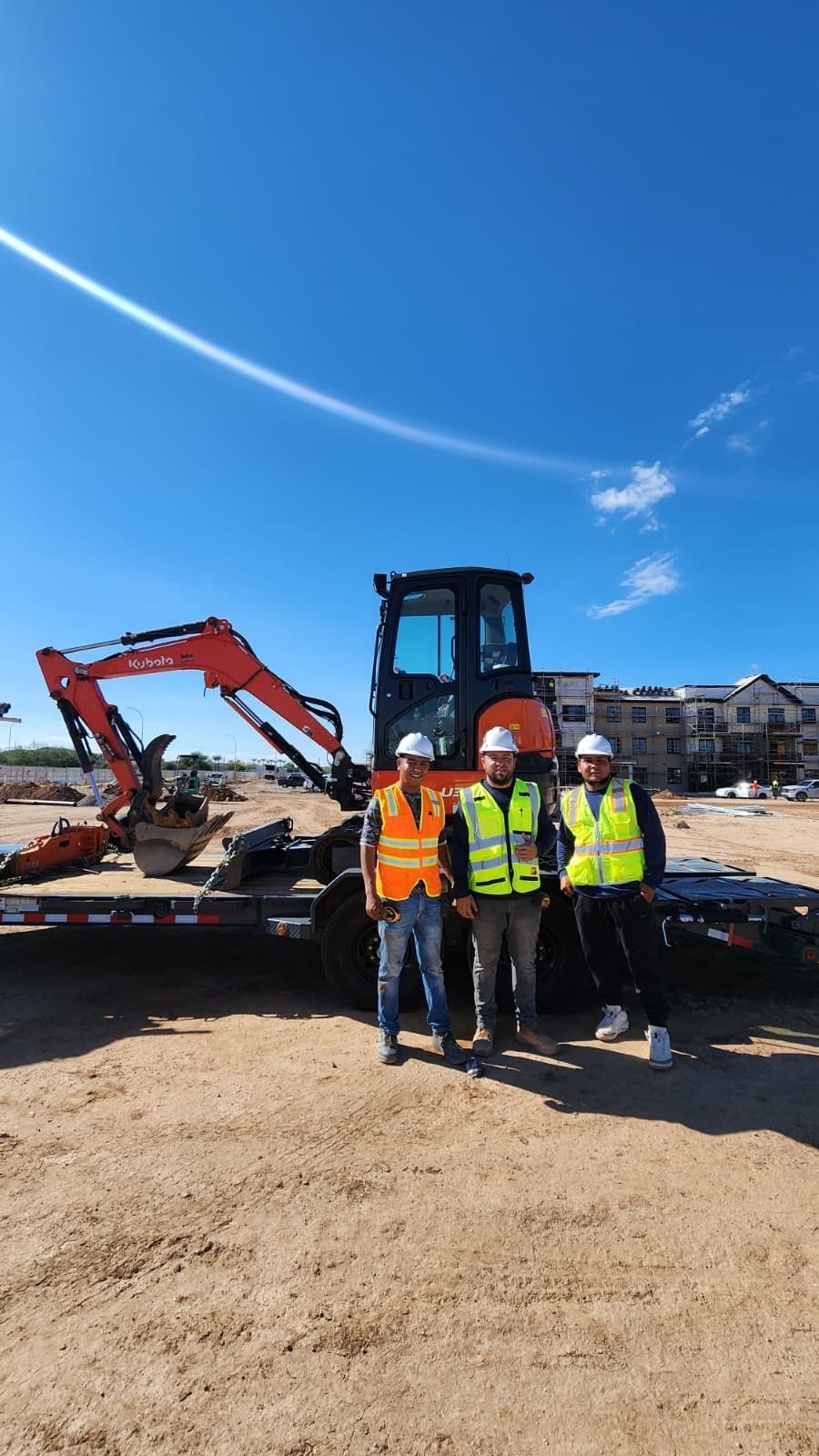 Four construction workers in safety vests stand before excavators at a building site.