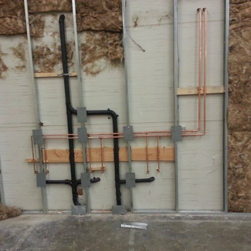 Exposed plumbing and electrical lines on a wall under construction, with copper and black pipes.