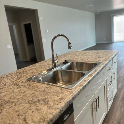 Kitchen island with granite countertop and stainless steel double sink and faucet in an empty room