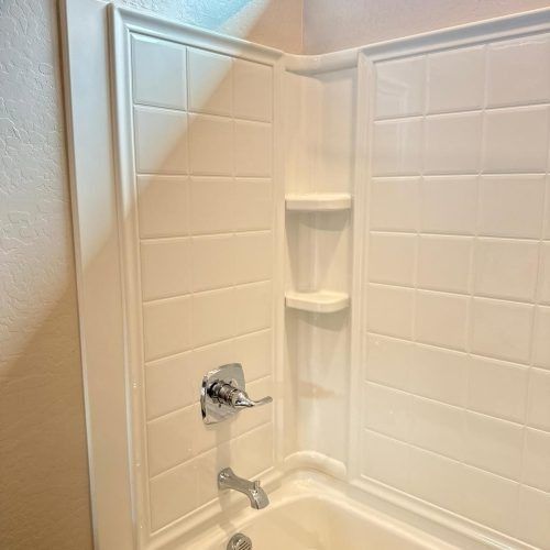 White tiled shower stall with built-in corner shelves and a chrome faucet