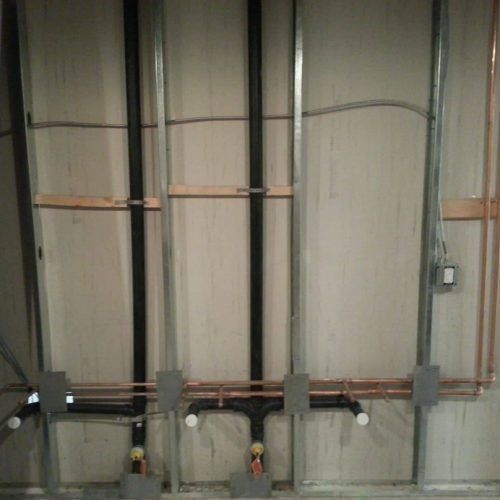 Industrial wall with exposed copper piping, valves, and electrical conduit on a metal-panel surface
