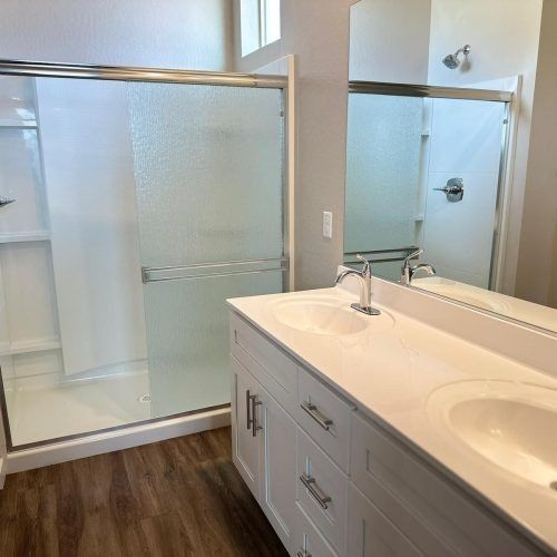 Modern bathroom with glass shower, double vanity, and wood-look floor