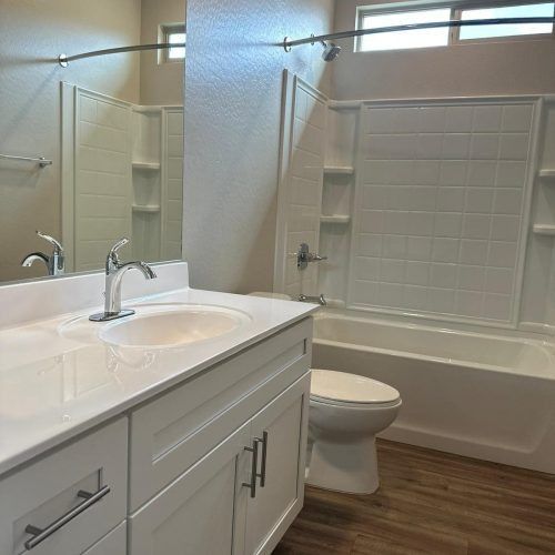 Clean white bathroom with double vanity, large mirror, and tub-shower combo with glass door.